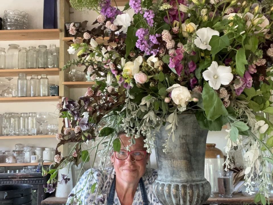 a tall vase full of a large flowering arrangement next to Georgie Newbery