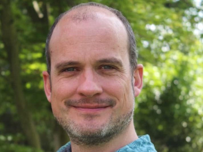 Matt Haddon headshot taken in a garden with trees in the background