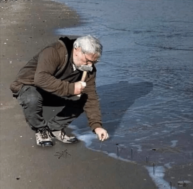 Guy hammering nails into sand at the beach Blank Template Imgflip
