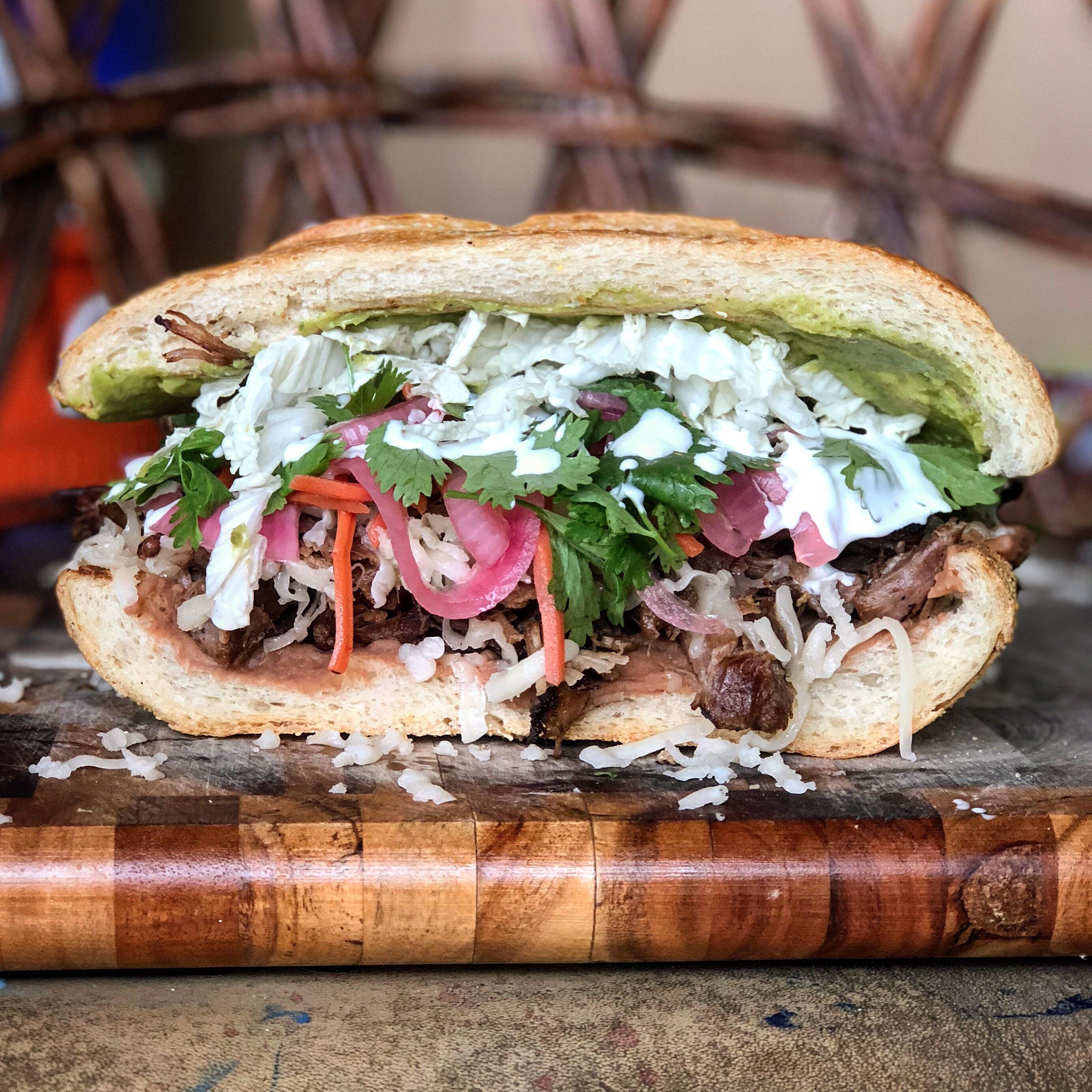 Carnitas Torta with pickled red onions and carrots, refried beans