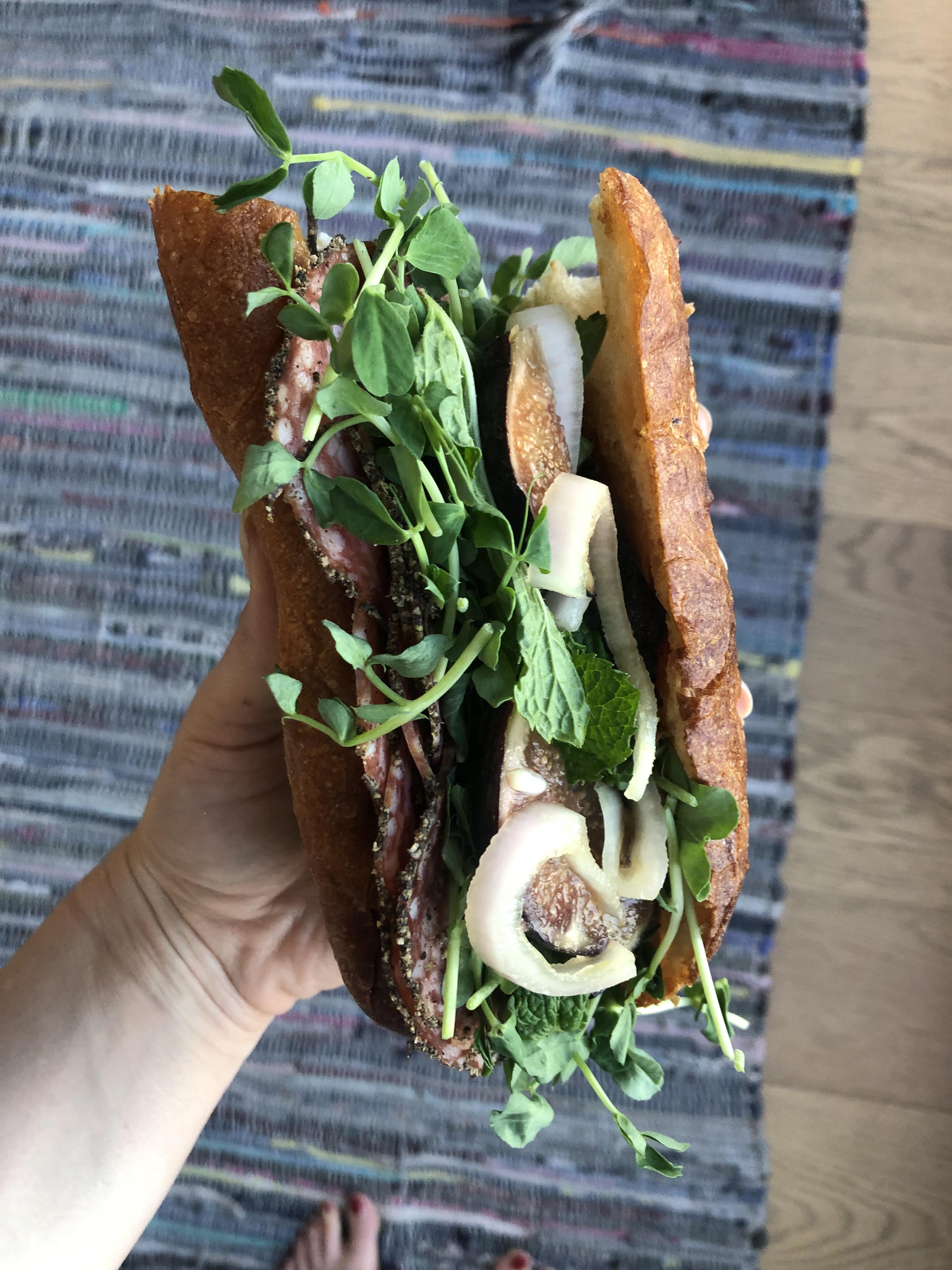 Salami, goat cheese, jam, pea shoots, mint, figs, and pickled shallots in a baguette r