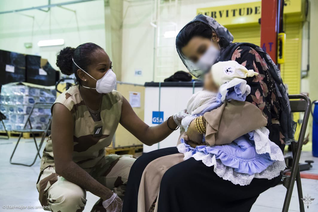 A member of the French Armed Forces Health Service checks on an Afghan evacuee and her baby, Al