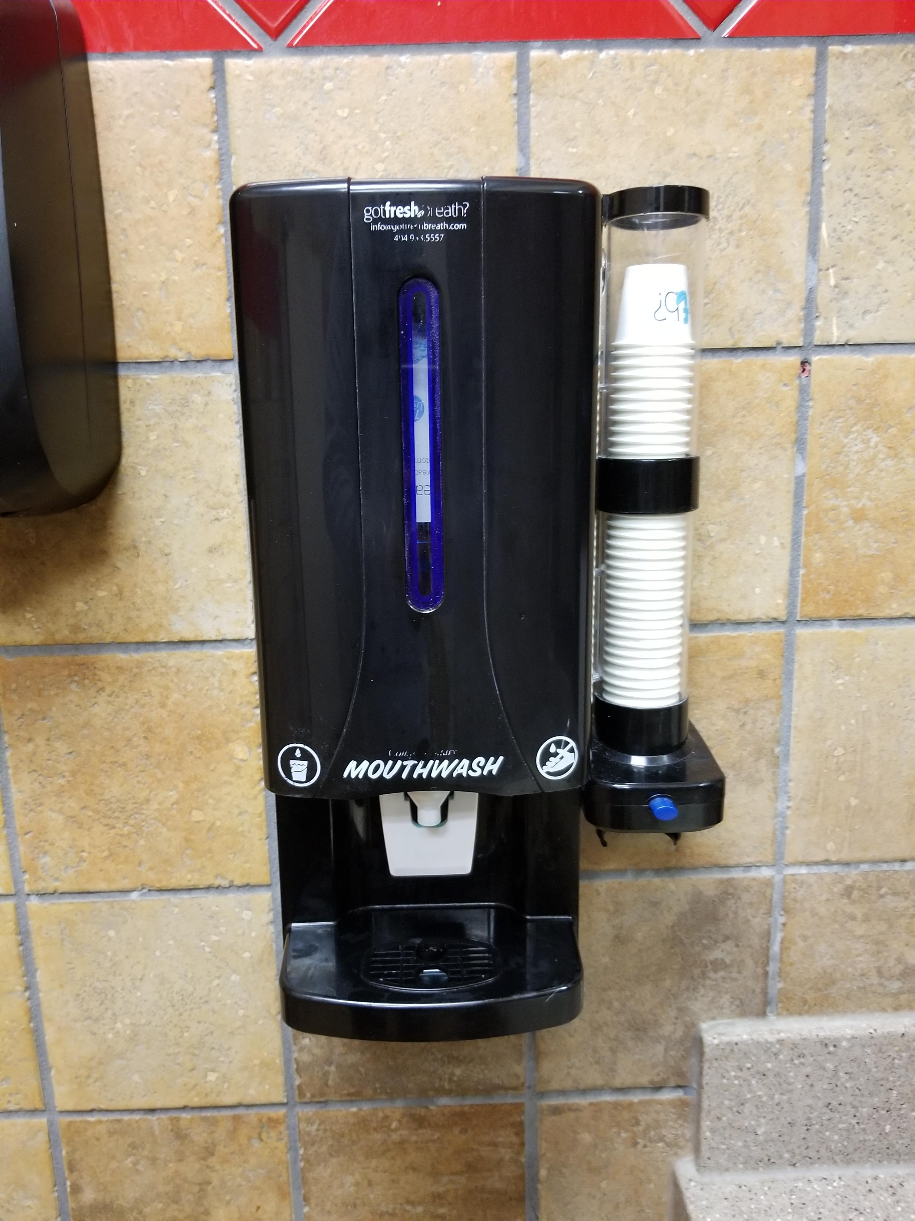 A mouthwash dispenser in the bathroom at a fast food restaurant. r