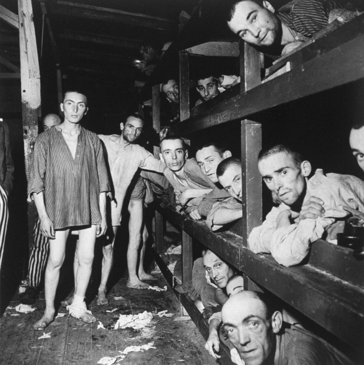 Emaciated male prisoners lying in bunks and standing halfnaked at Buchenwald concentration camp