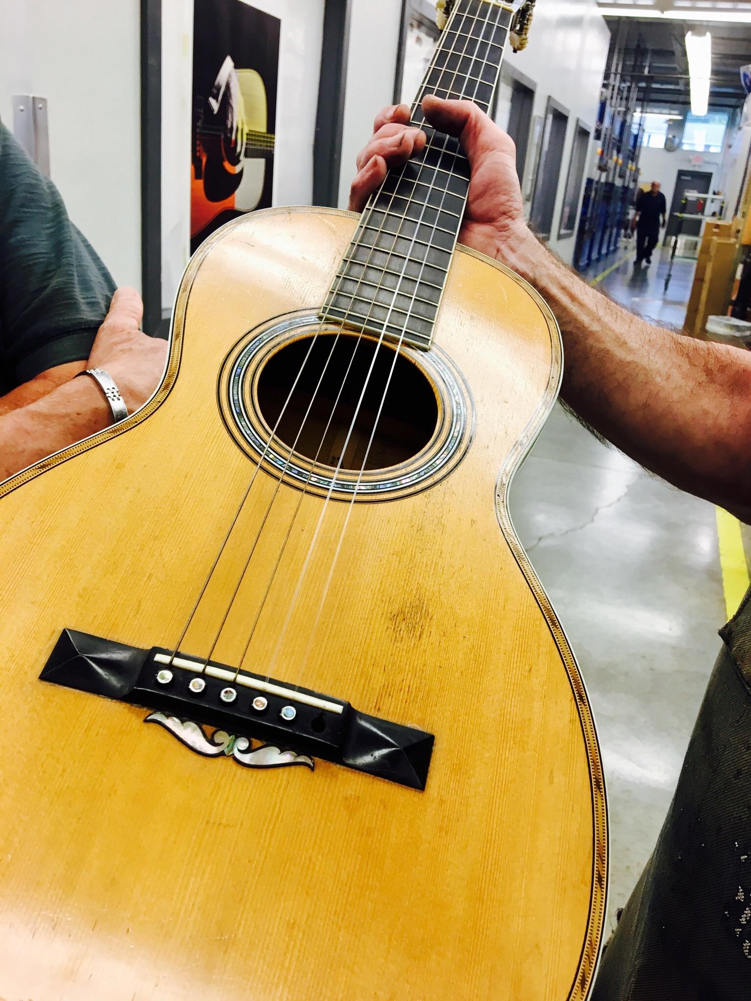 Martin factory repair shop; repair technician showing tour members a customer guitar sent in for