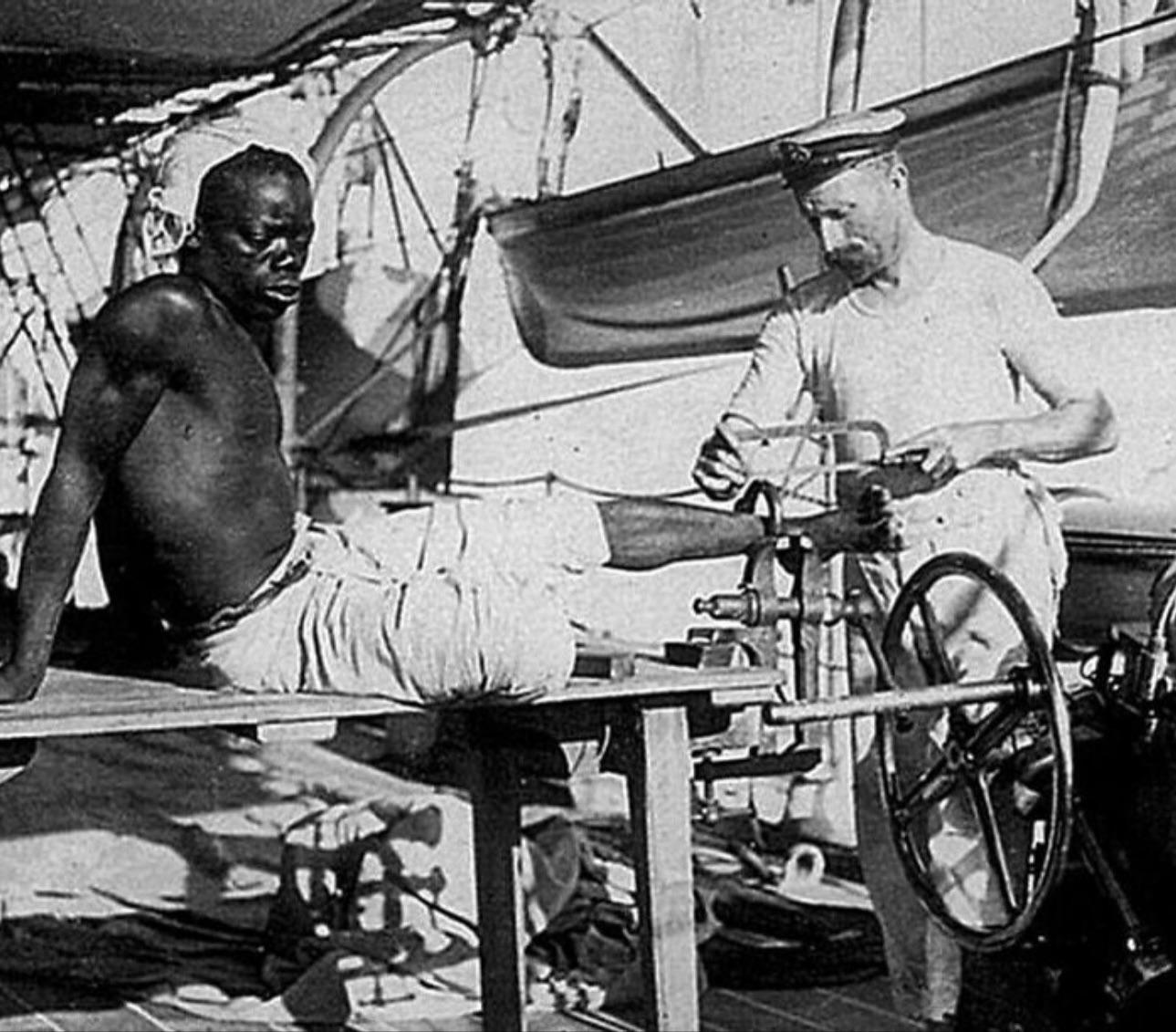 A British blacksmith removing the leg irons off a slave in 1907 off the coast Of Mozambique.