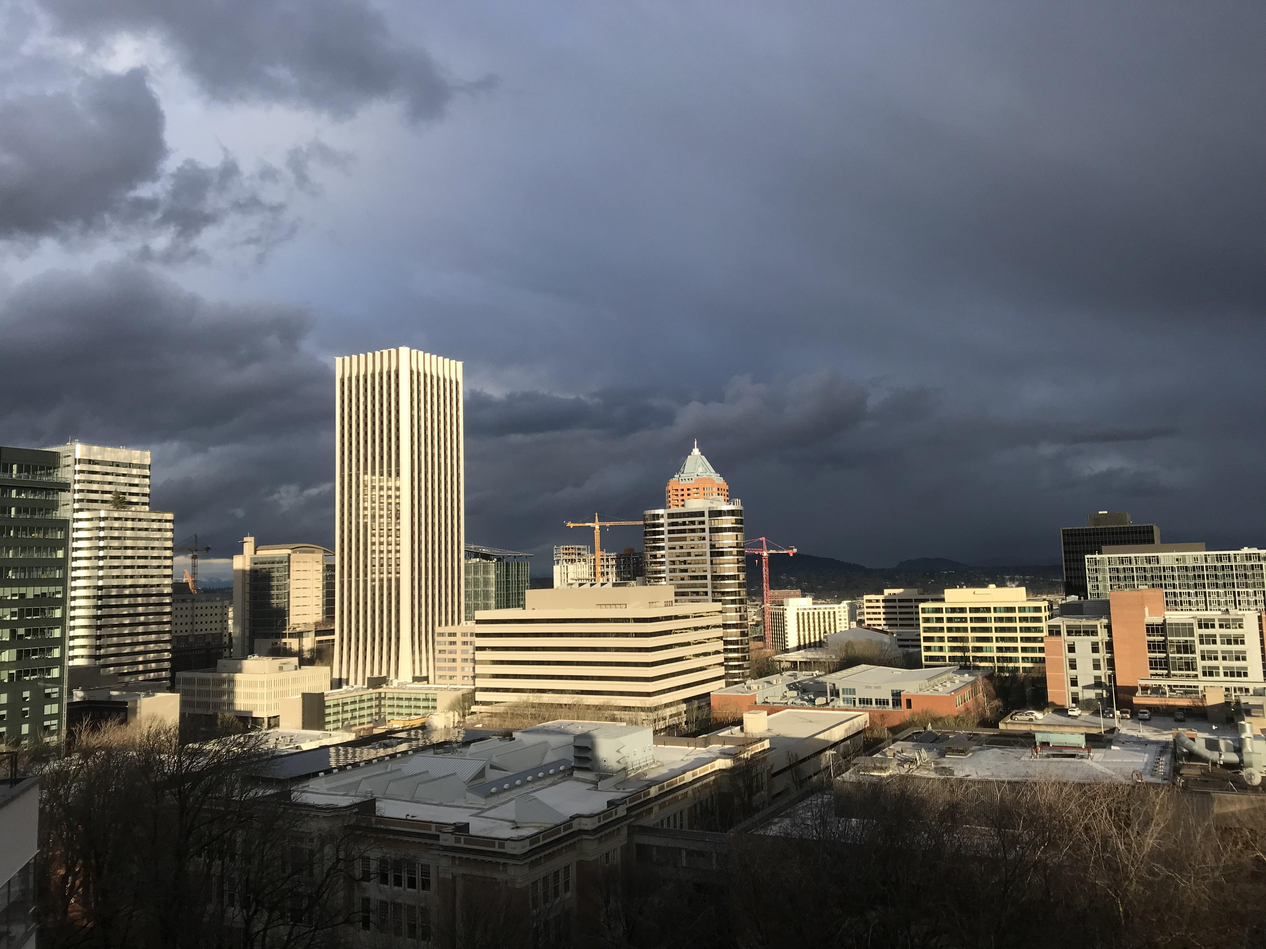 Sunlit downtown against stormy skies r/Portland