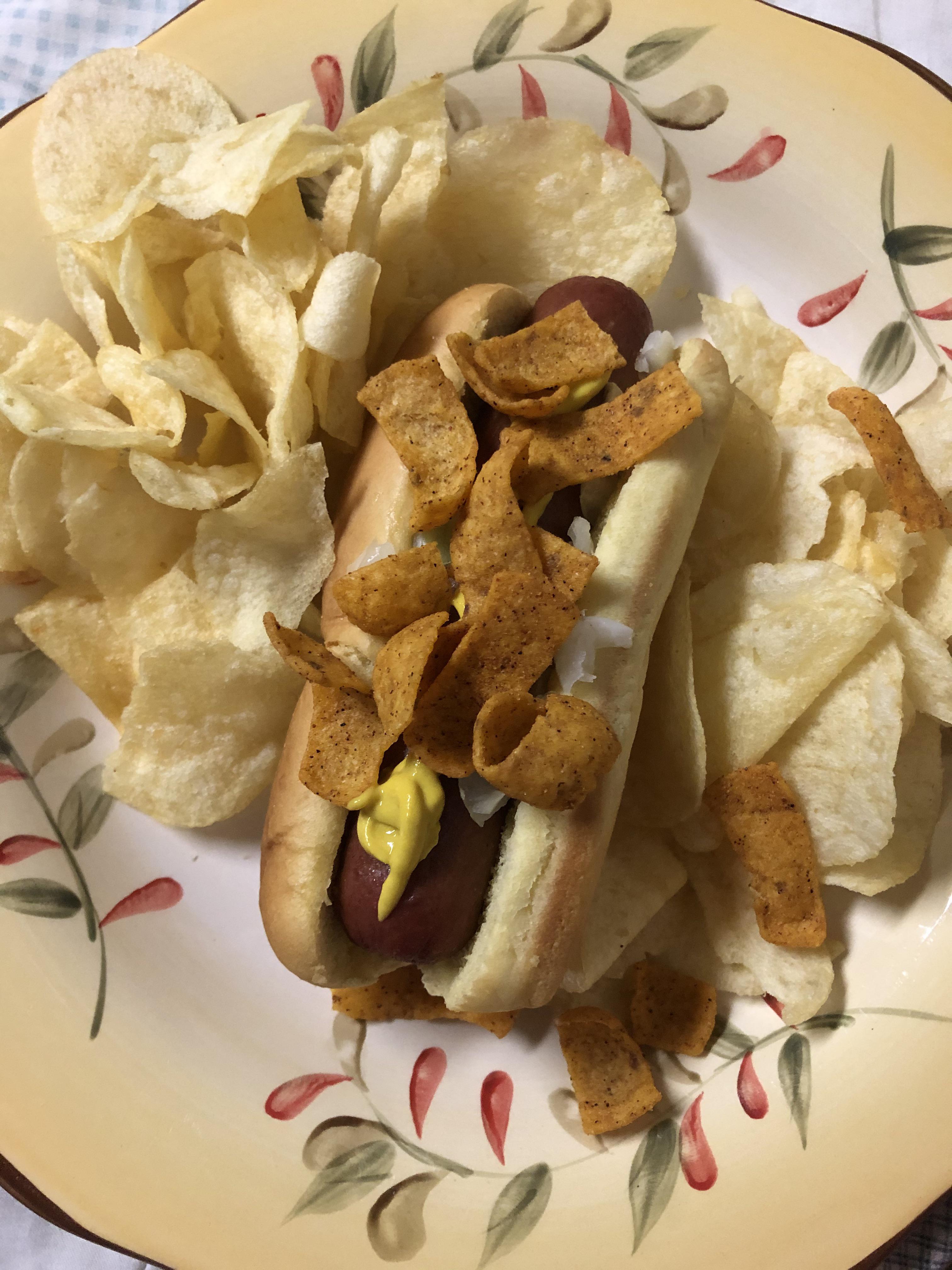 Reheated hot dog with chili cheese Fritos on top, lays on the side r