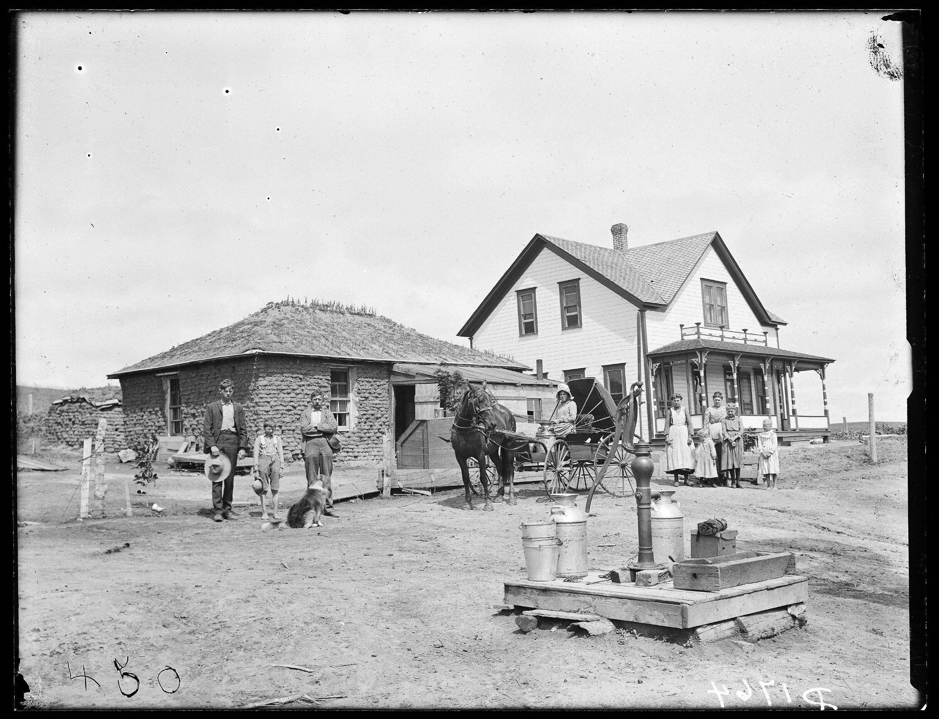 A sod house next to a wooden house, and the family that lives in them