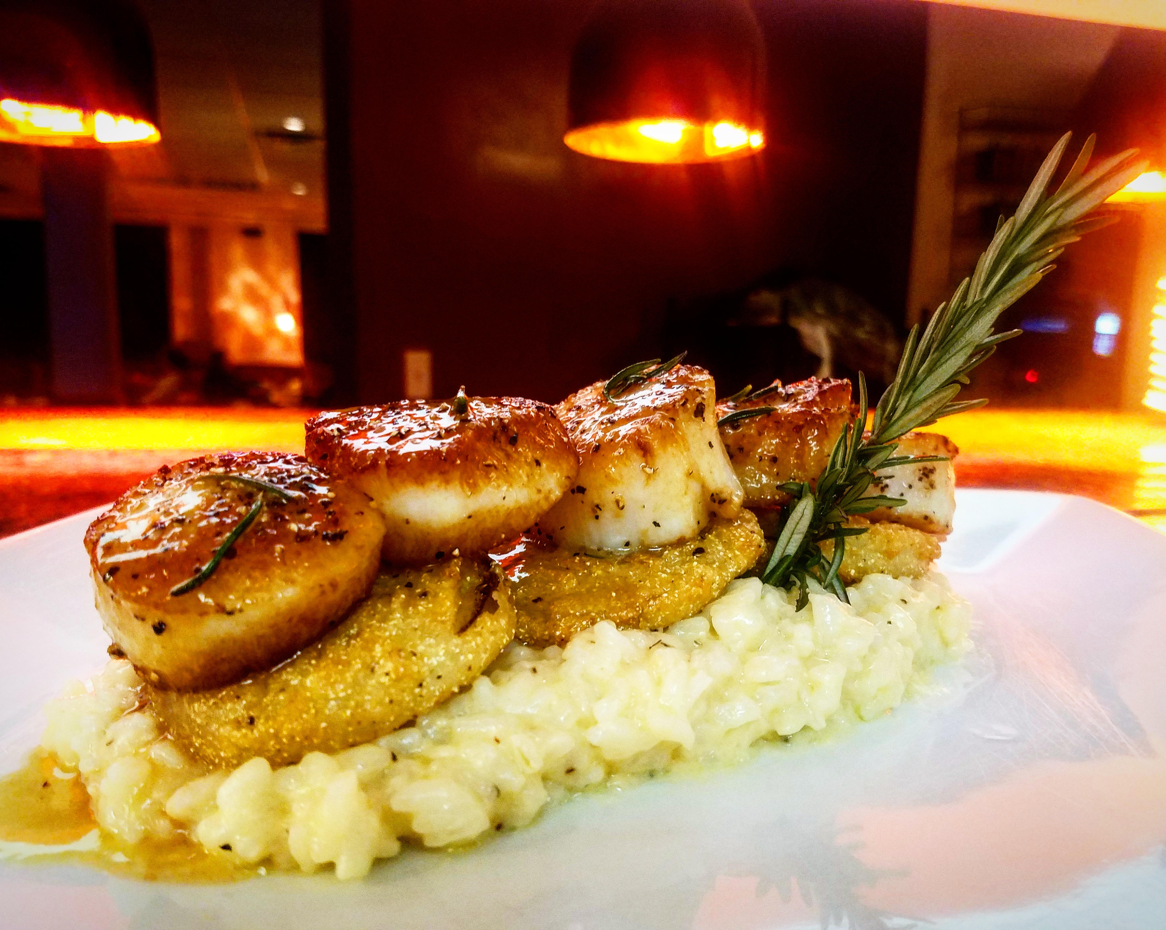 Scallops over fried green tomatoes and parmesan risotto, topped with