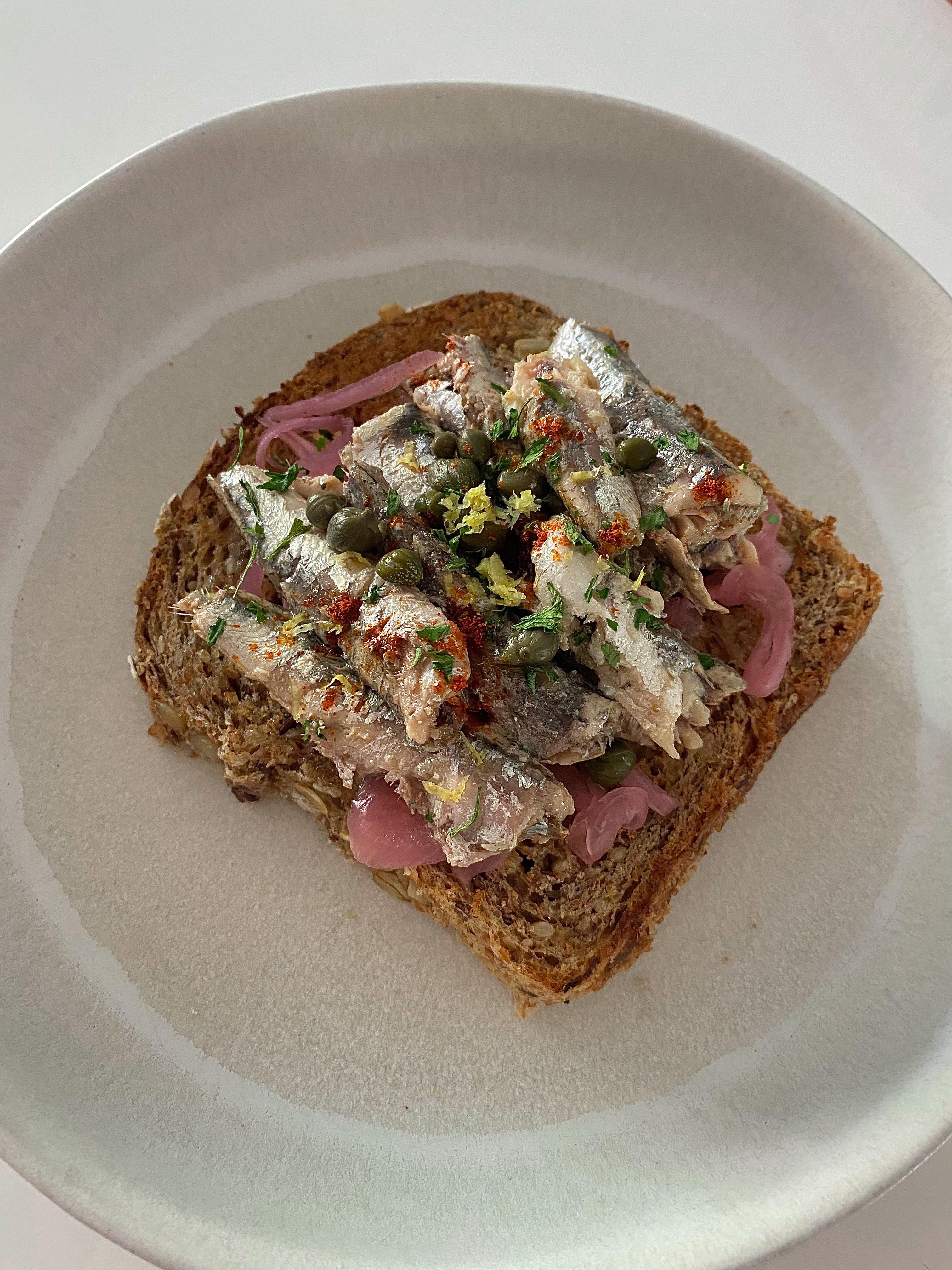 White anchovies on toast with pickled onions and capers, topped with paprika, parsley and lemon