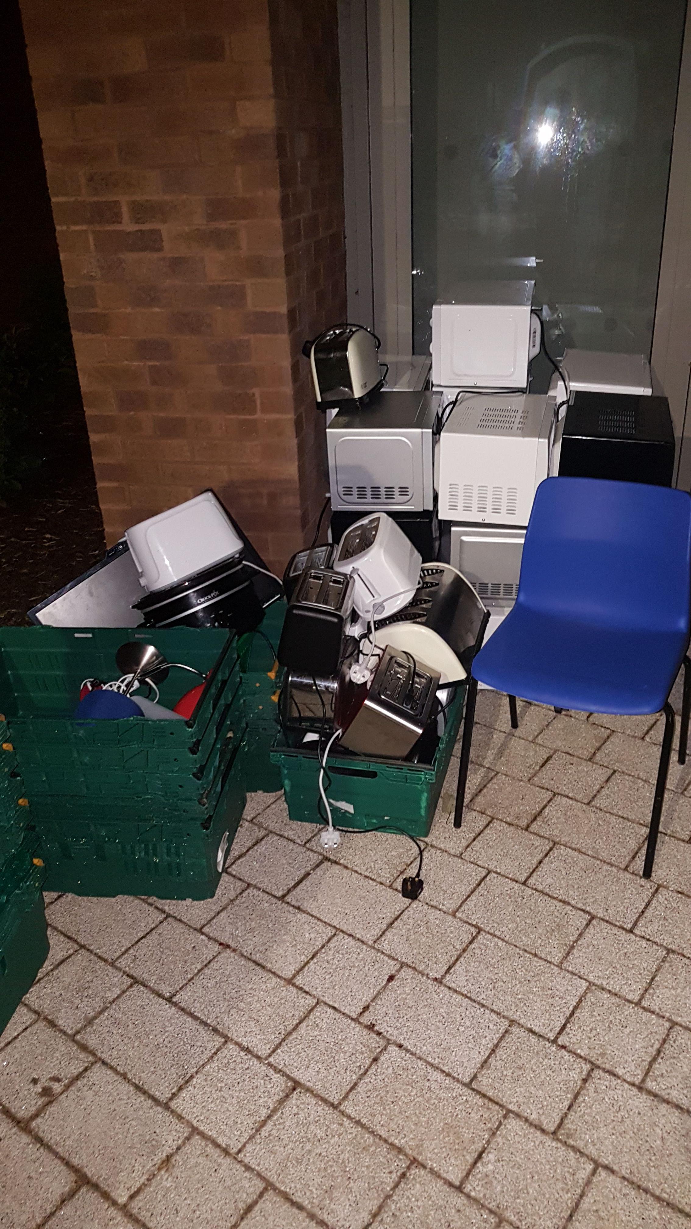 Microwaves, toasters, lamps and a TV, all next to college dorms. r