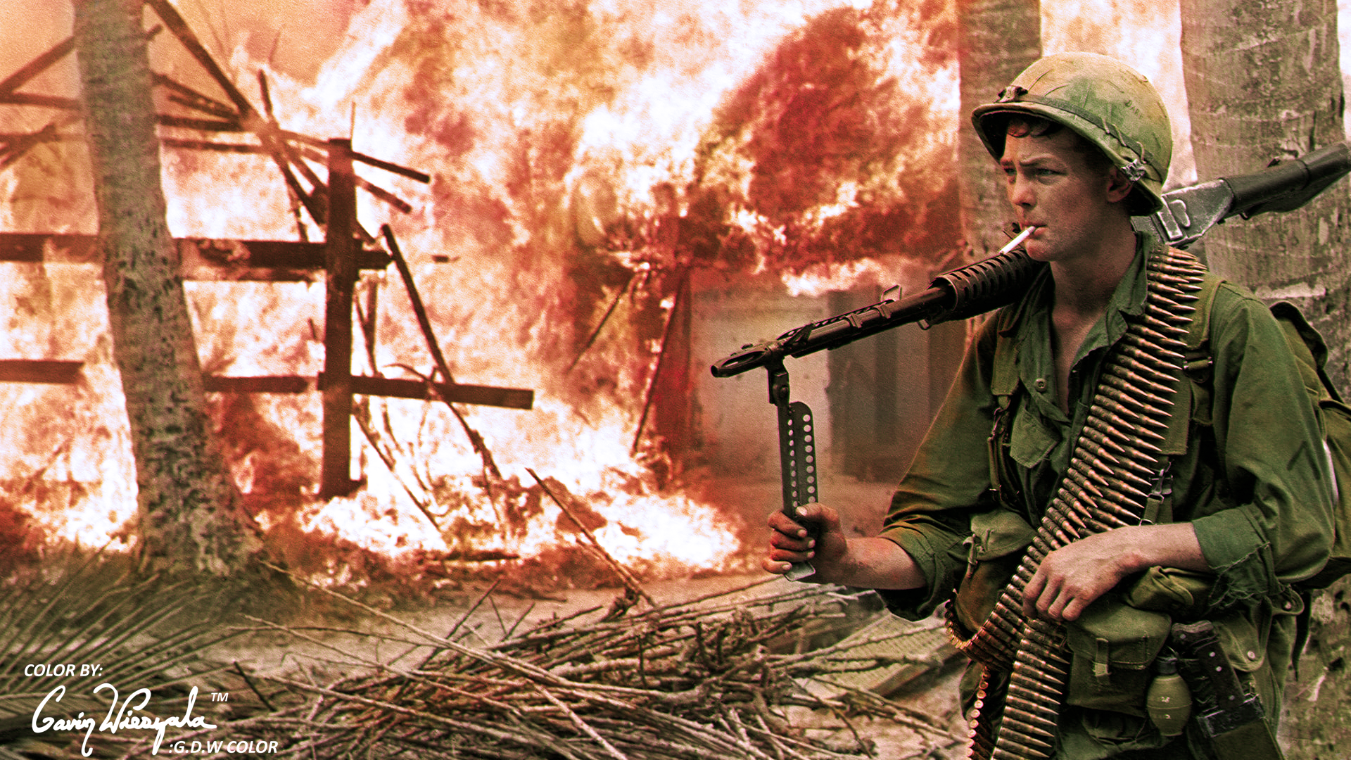 A US soldier with an M60 passes by a blazing village. Vietnam War. r