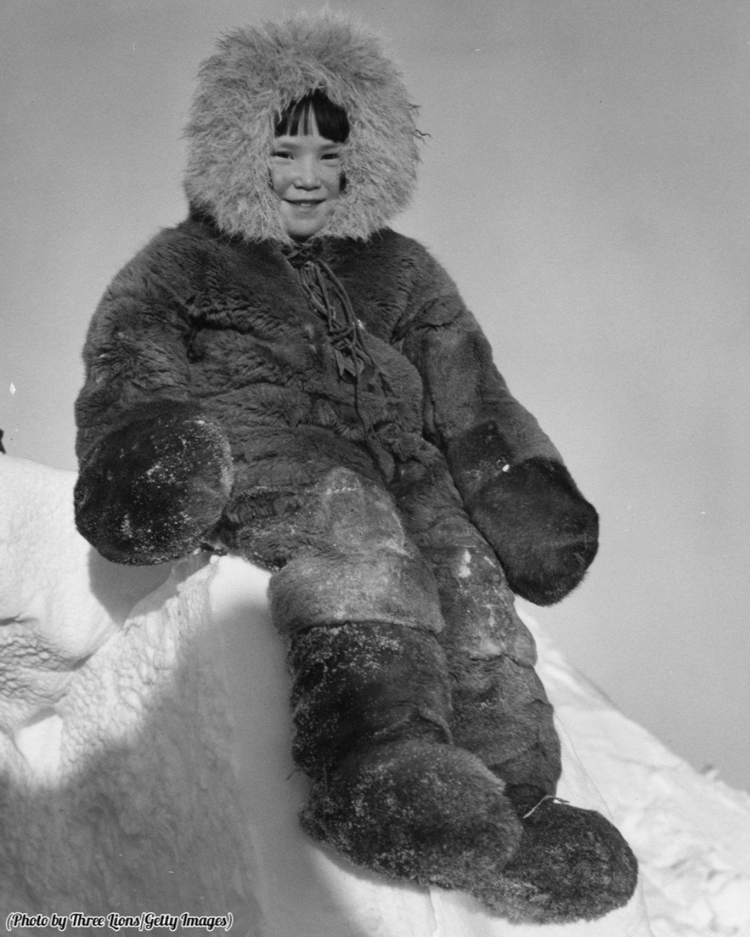 A young Inuit girl bundled up in traditional winter clothing, circa