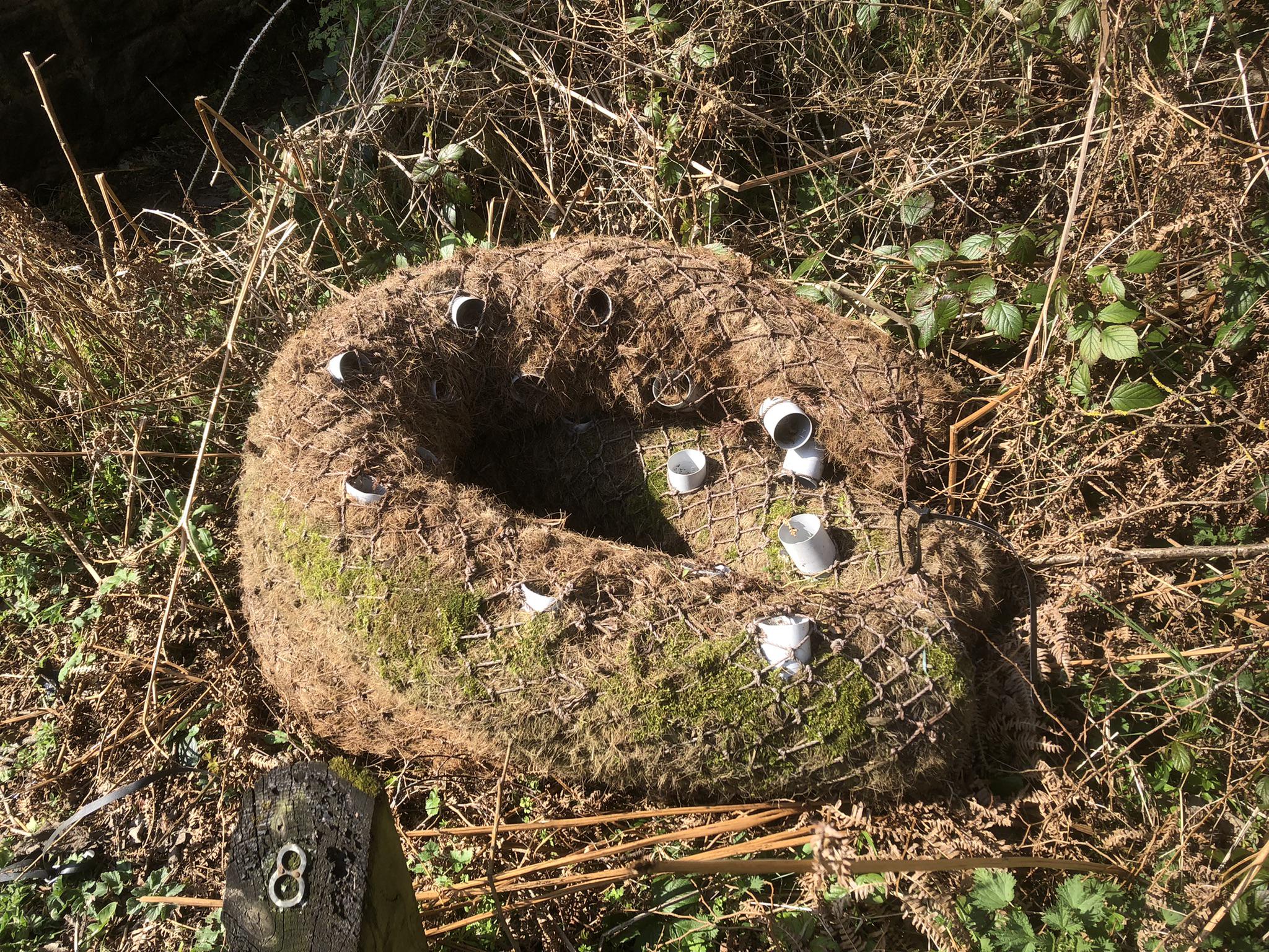 Netting filled with natural materials (dirt, grass) and short pieces of PVC pipe stuck, bent