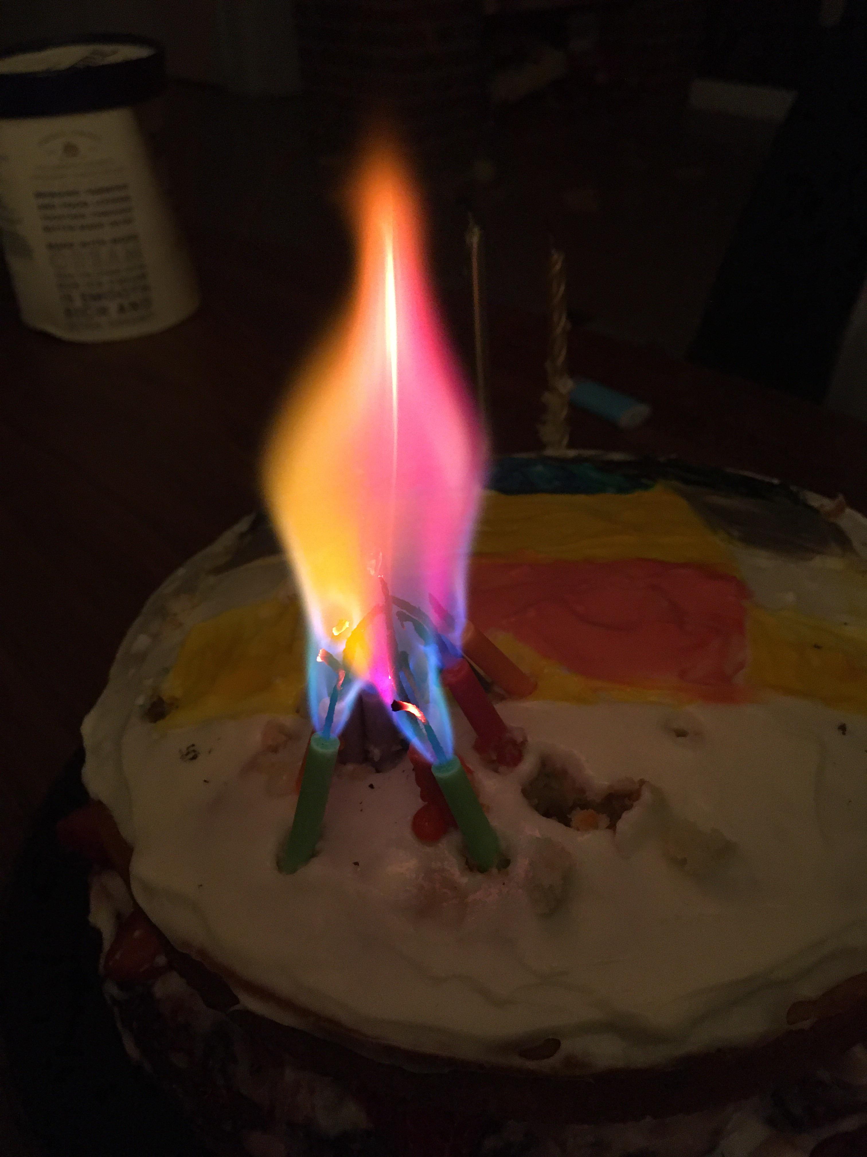 Colored candles all bunched up together make one big rainbow flame r