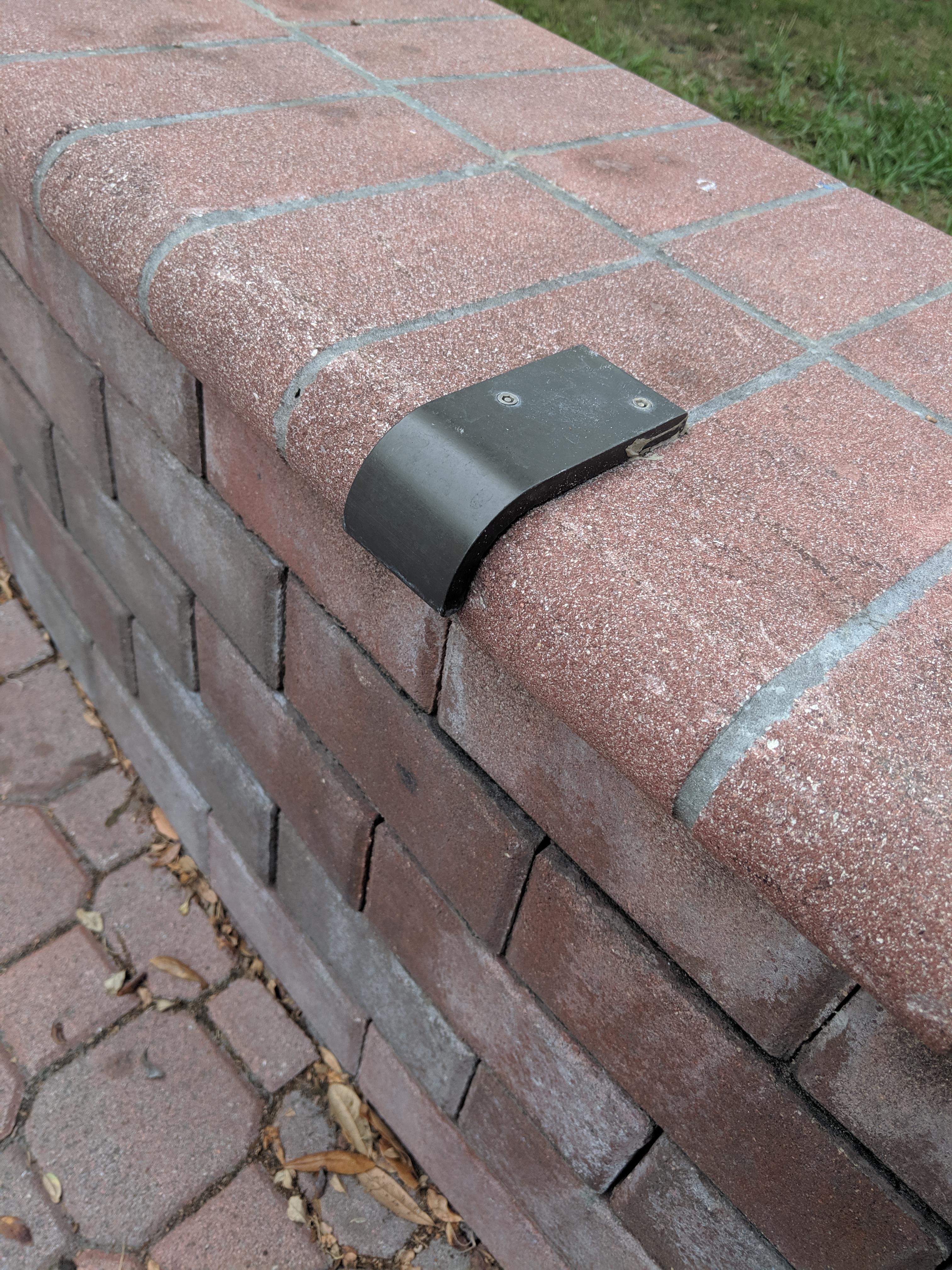 Metal piece fastened by screws on a small brick wall. Nothing visible