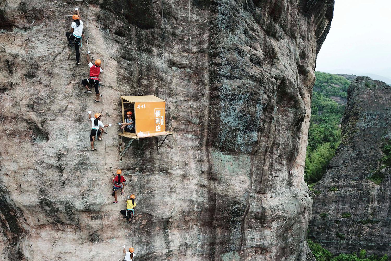 People climb on a cliff face past a 100meterhigh convenience store in