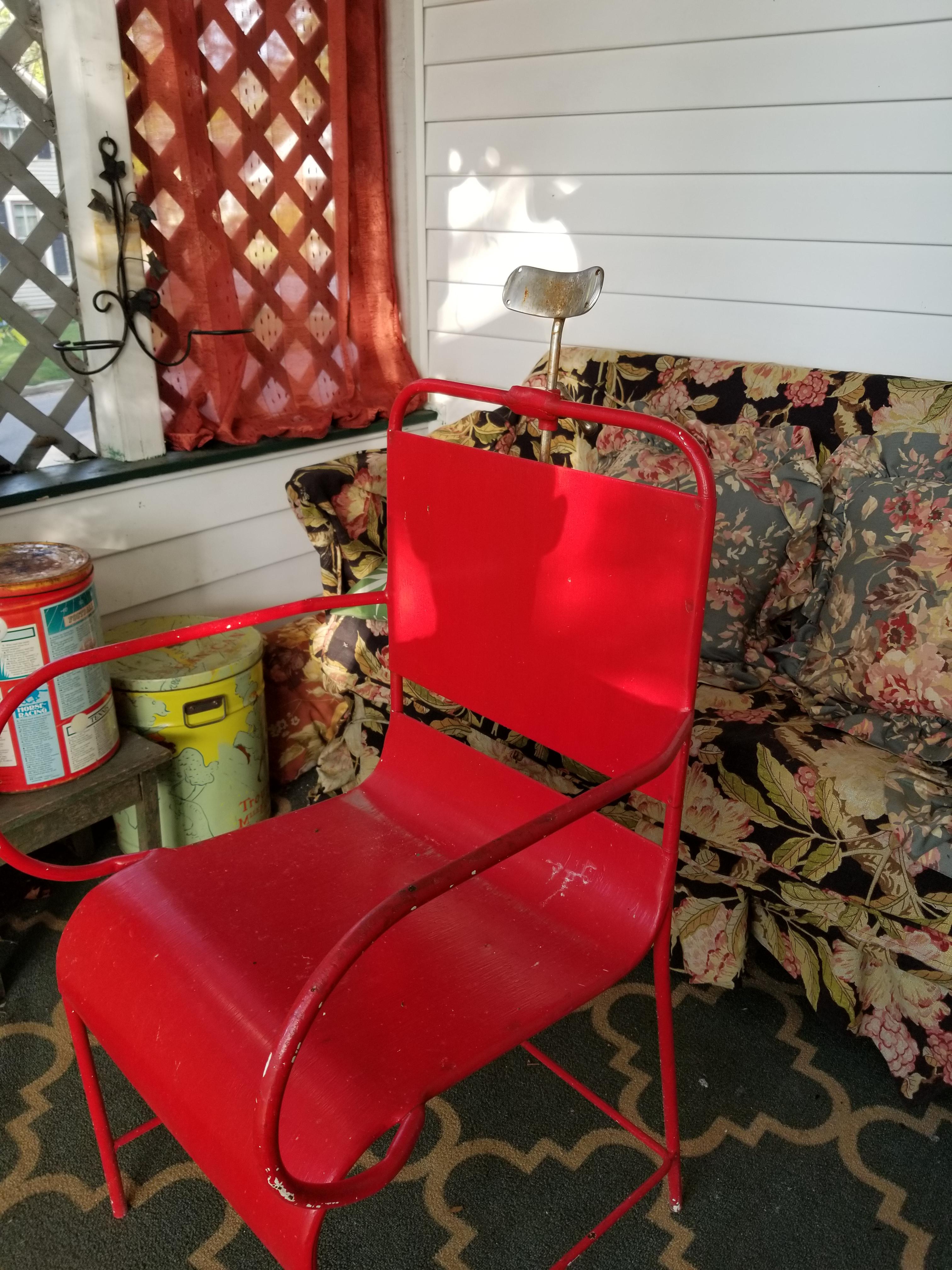 Red metal chair with adjustable metal headrest and legs with holes in