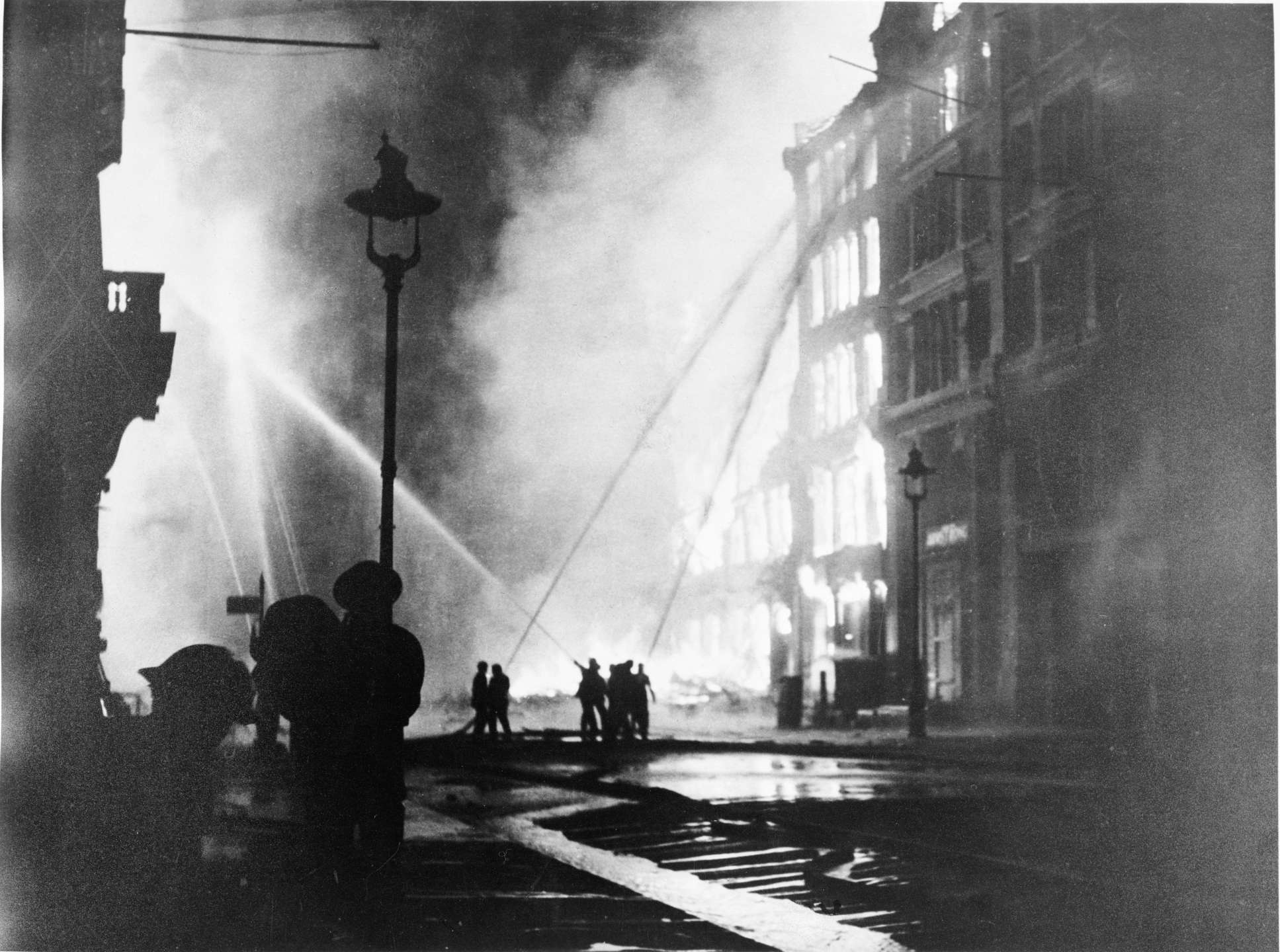 British firemen of the London Fire Brigade train hoses on burning