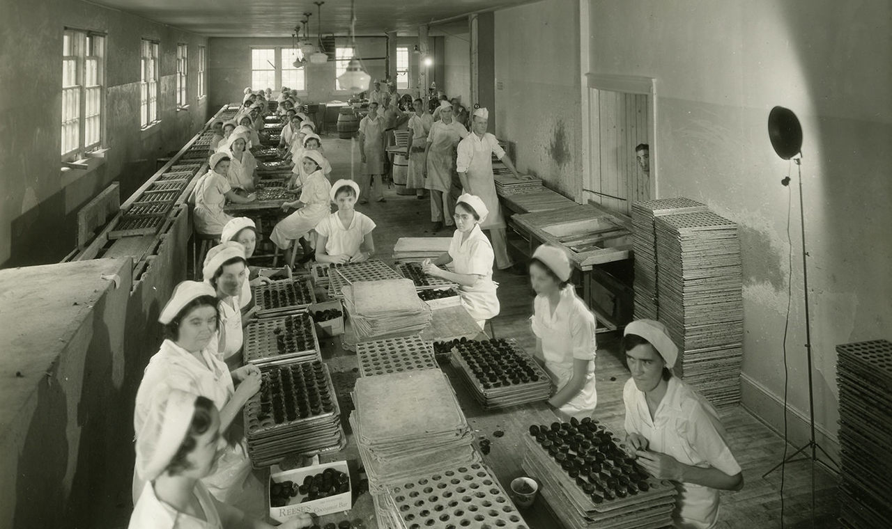 Factory workers cupping and dipping Reese's peanut butter cups by hand before machines