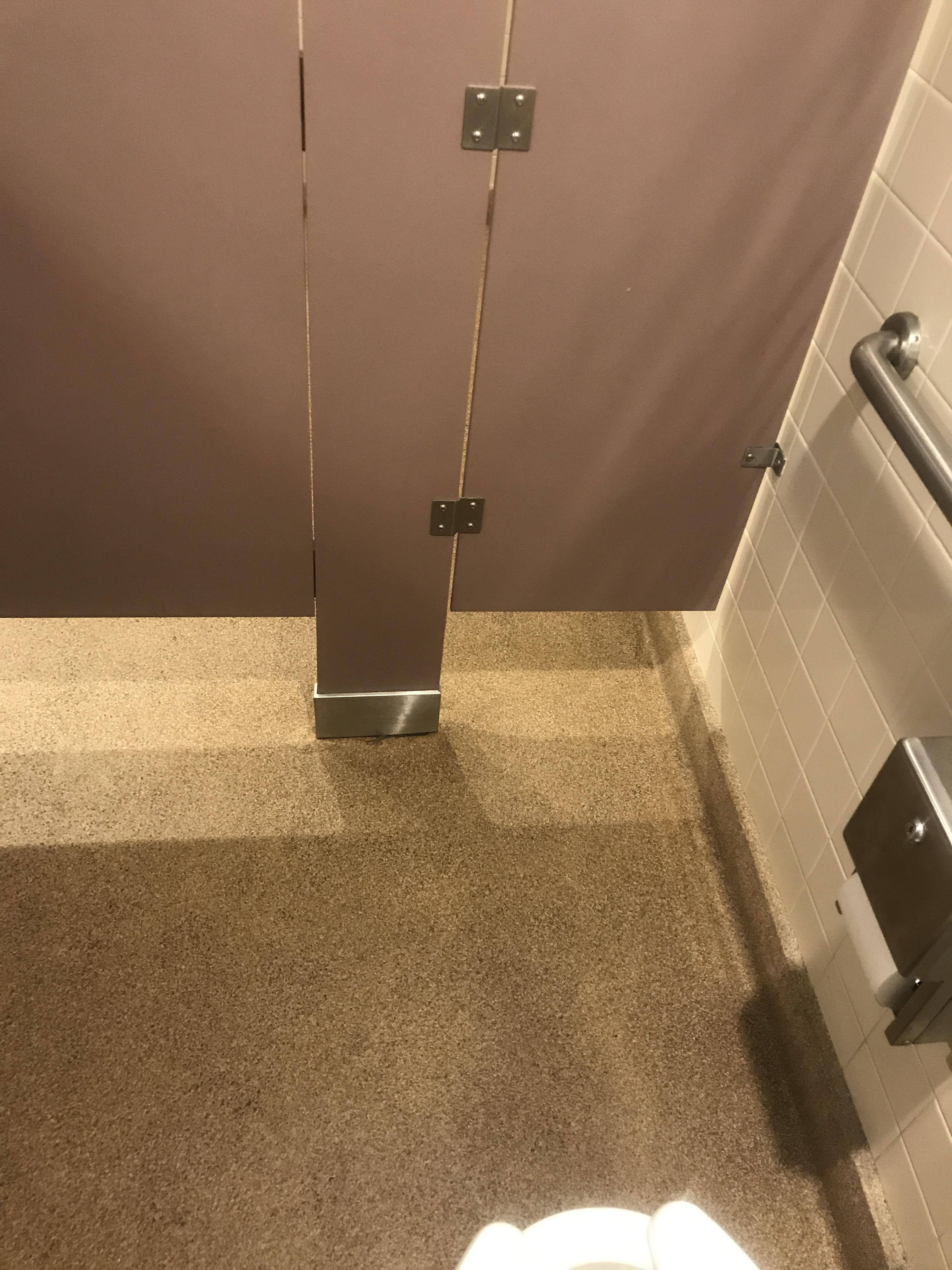 A crack in the wall of this bathroom stall is in front of the toilet