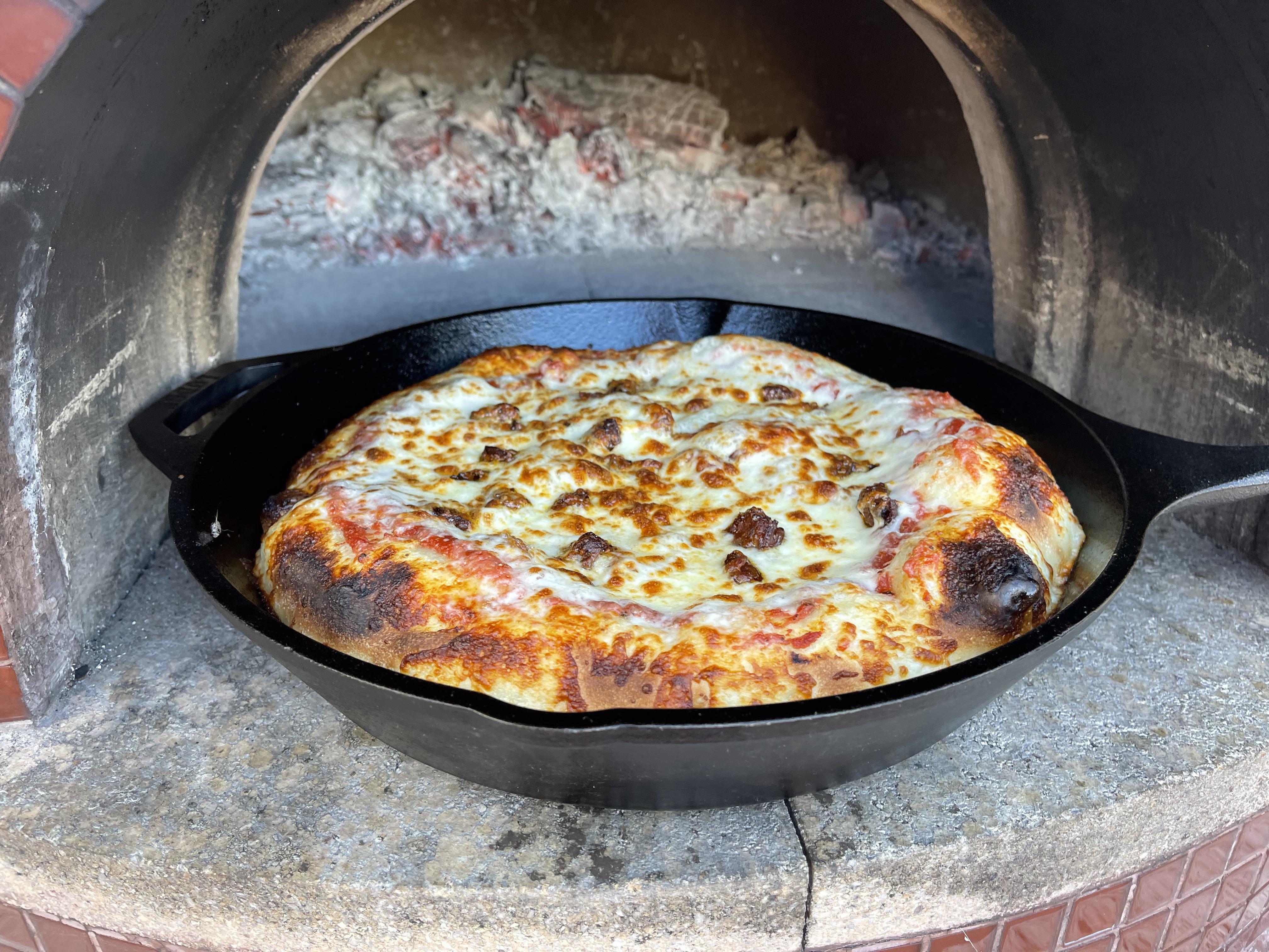 Cast iron pizza in the pizza oven with bacon, pepperoni, sausage, and