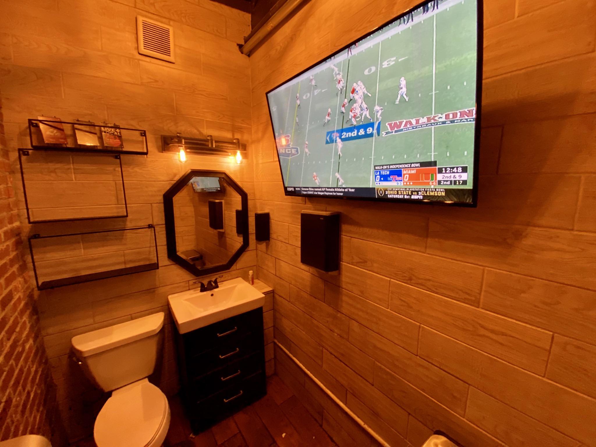 This bar has a single person bathroom with a giant TV in it. r
