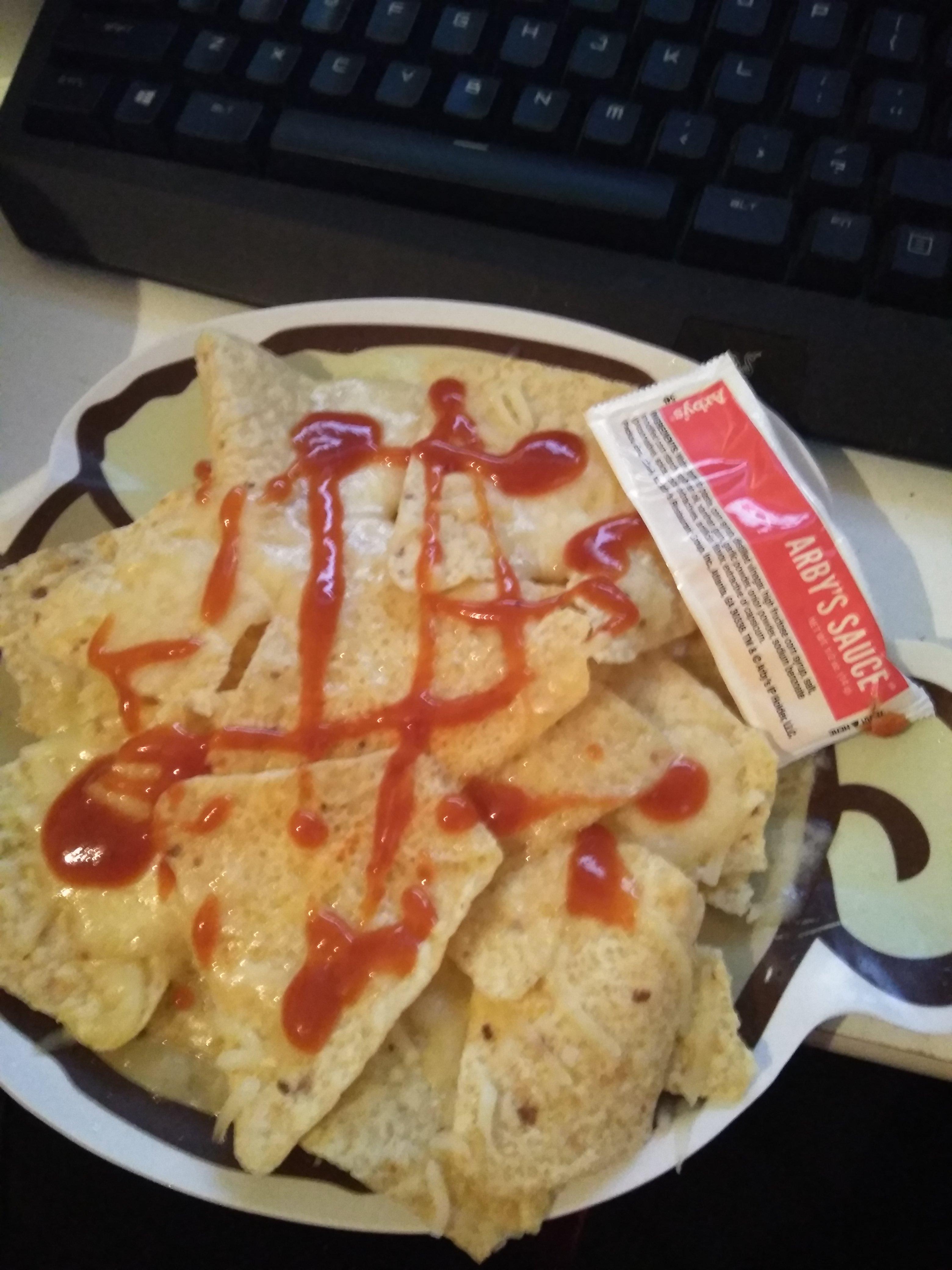 Shredded cheese microwave nachos with arby's sauce on top on a