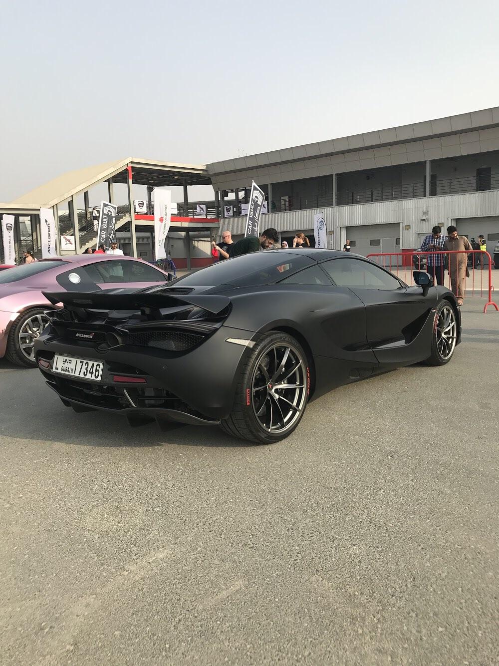 A matte black McLaren 720S with red inscription on the tires at a car
