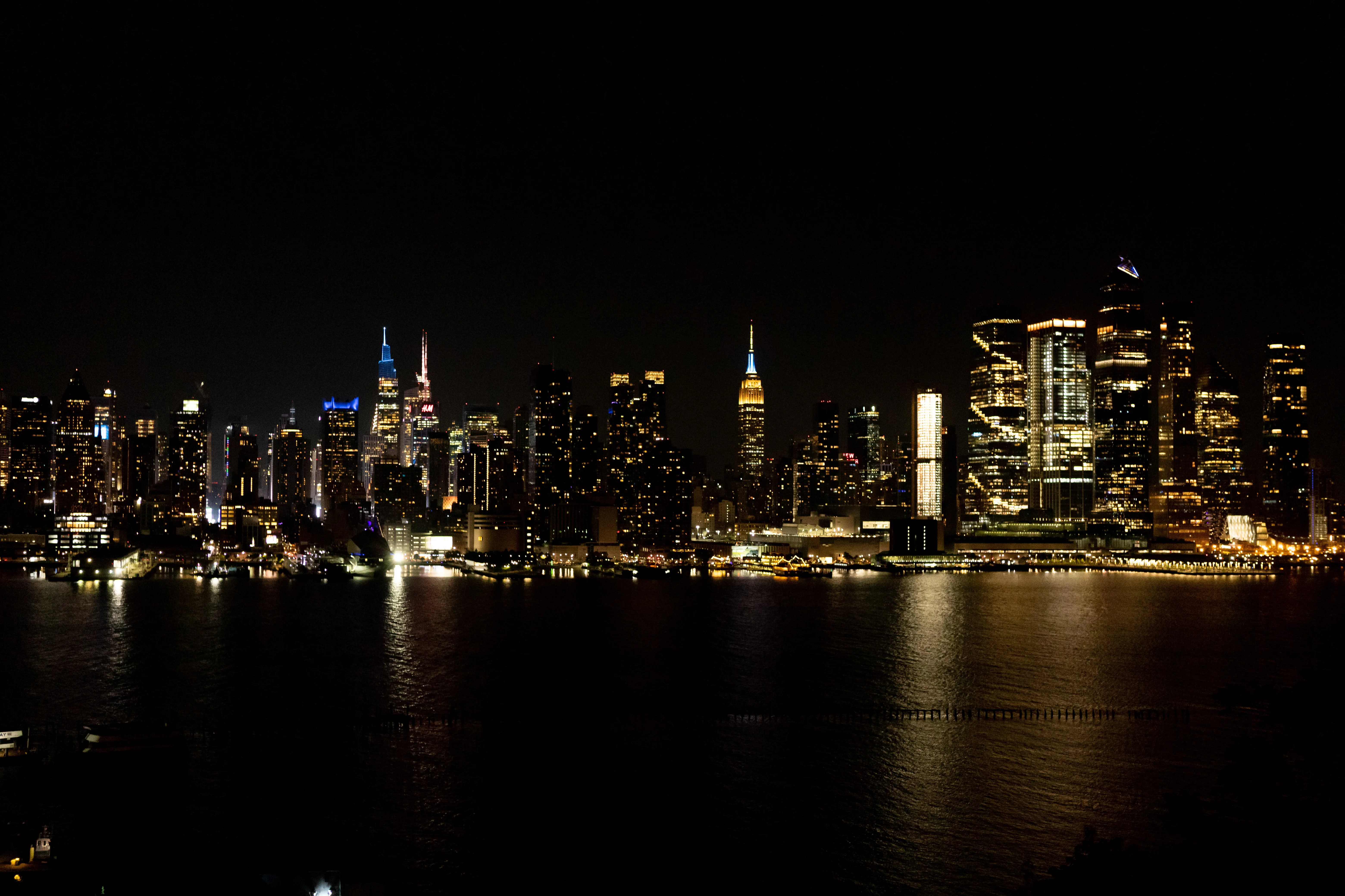 Stunning nighttime view of New York City's illuminated skyline reflecting on the water, featuring iconic landmarks.