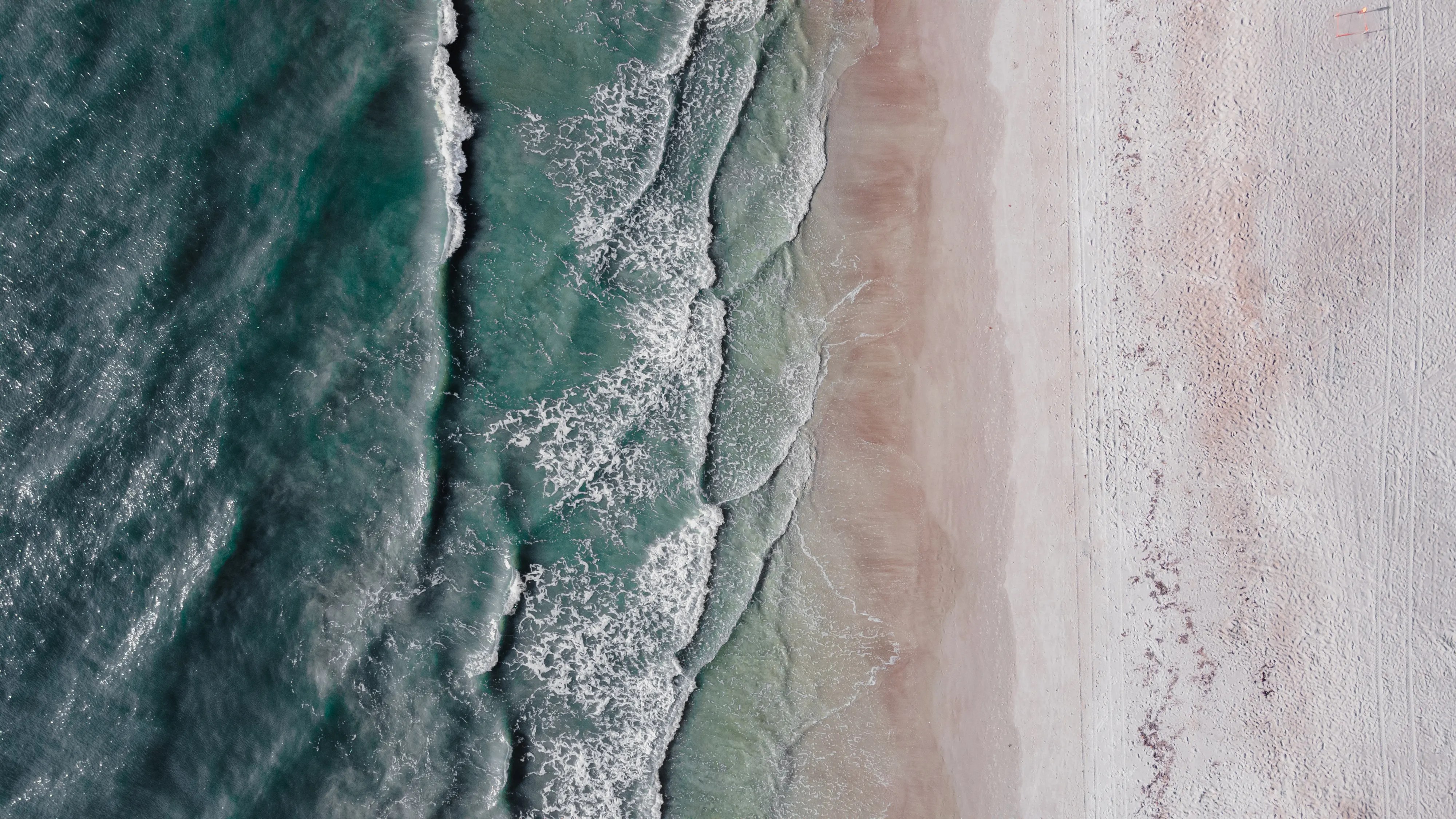 Stunning aerial view of turquoise waves crashing on a sandy beach, offering a tranquil seaside scene.