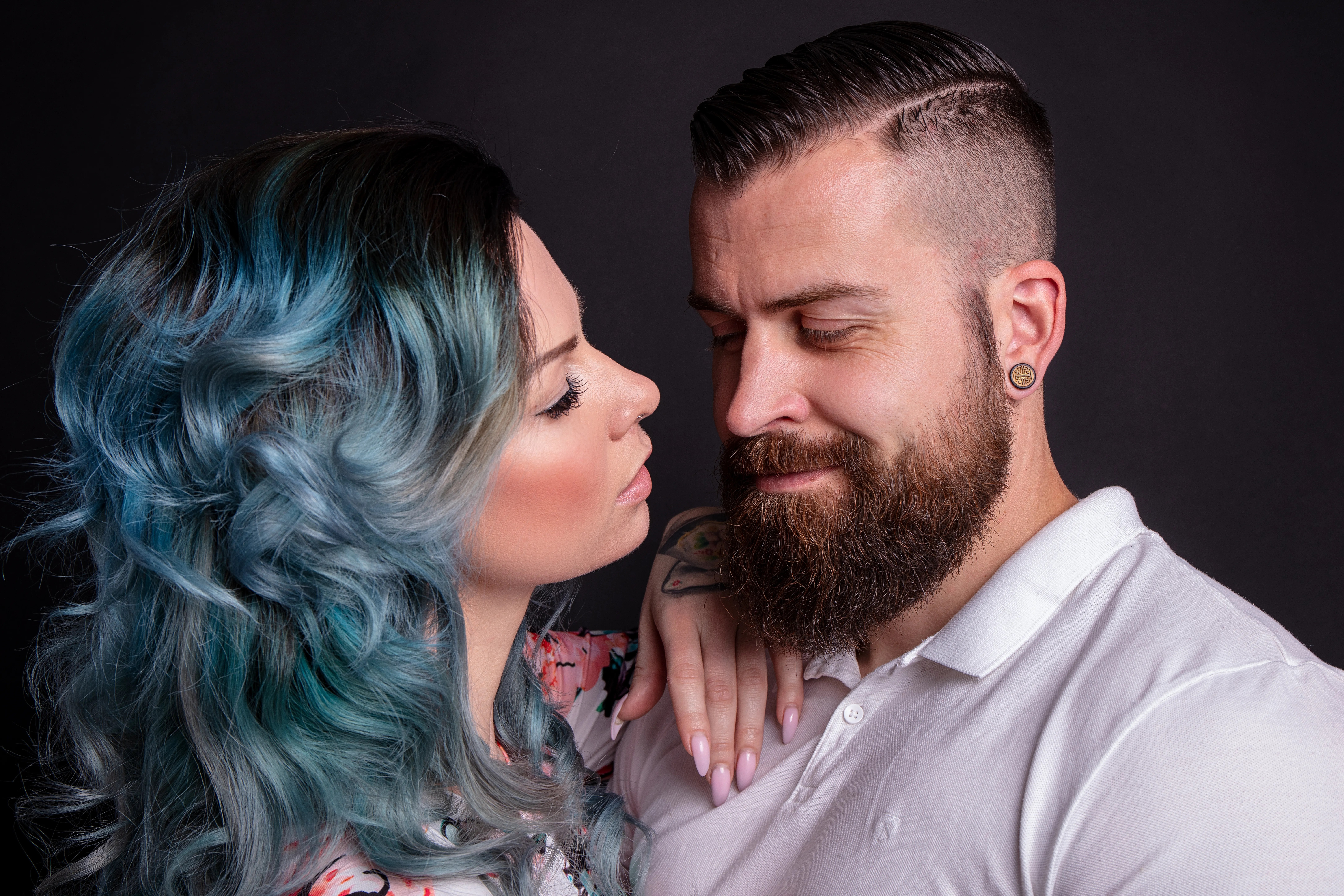 Intimate studio portrait of a loving couple sharing an affectionate moment against a black background.