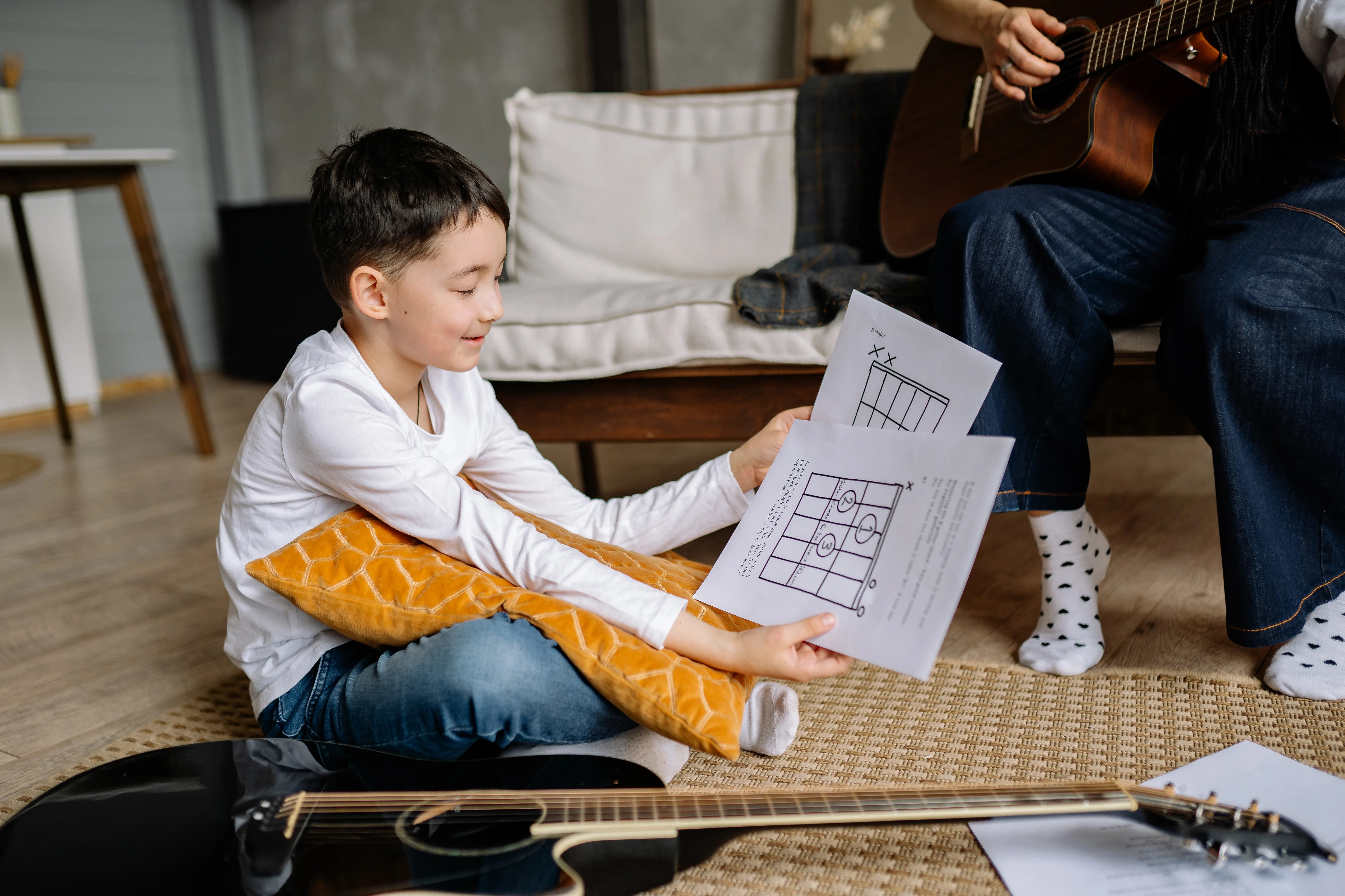 A young boy learning guitar indoors with sheet music, highlighting musical education.