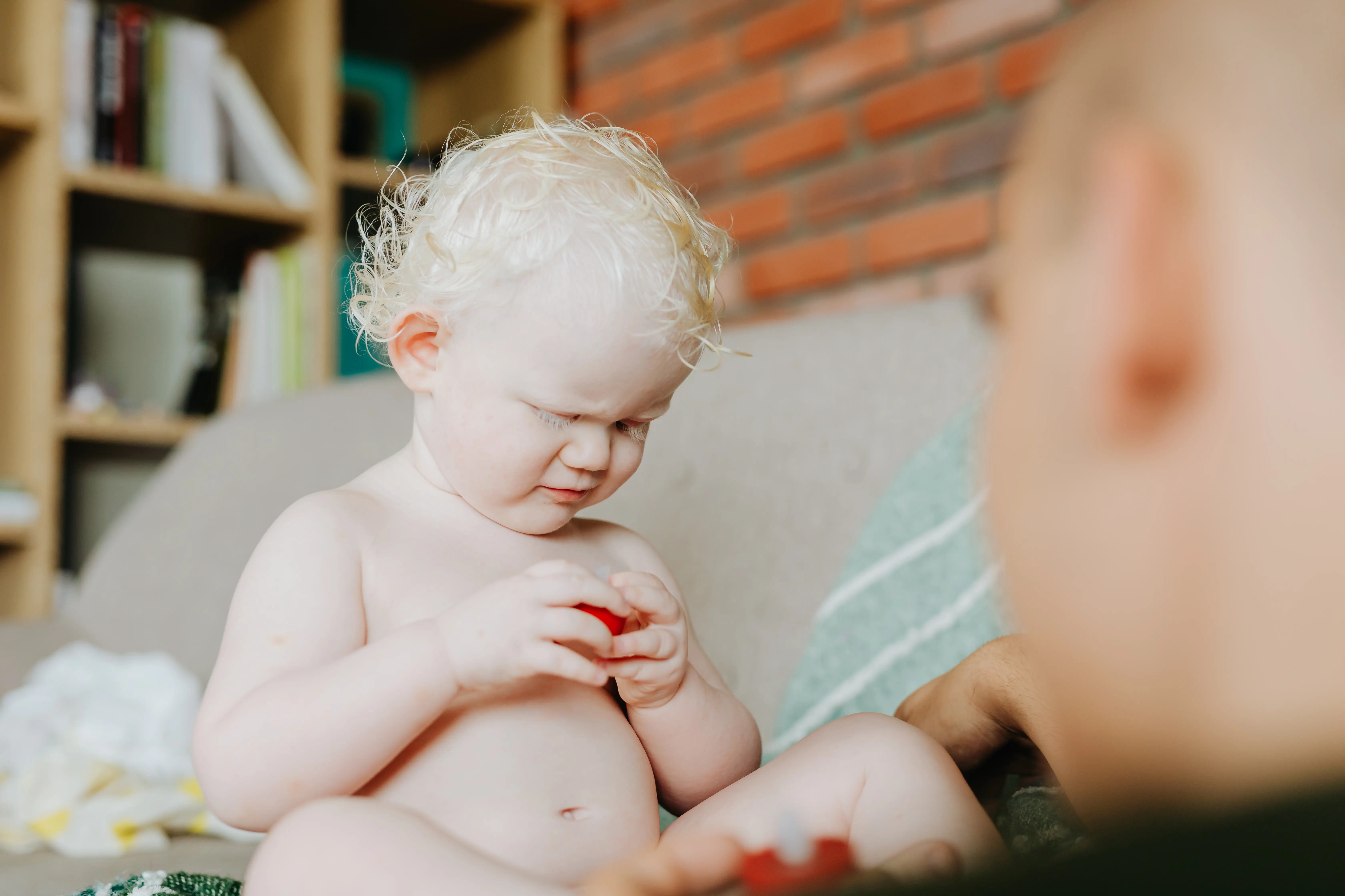 Adorable baby with white hair engrossed in play indoors, showcasing innocence and curiosity in a cozy setting.