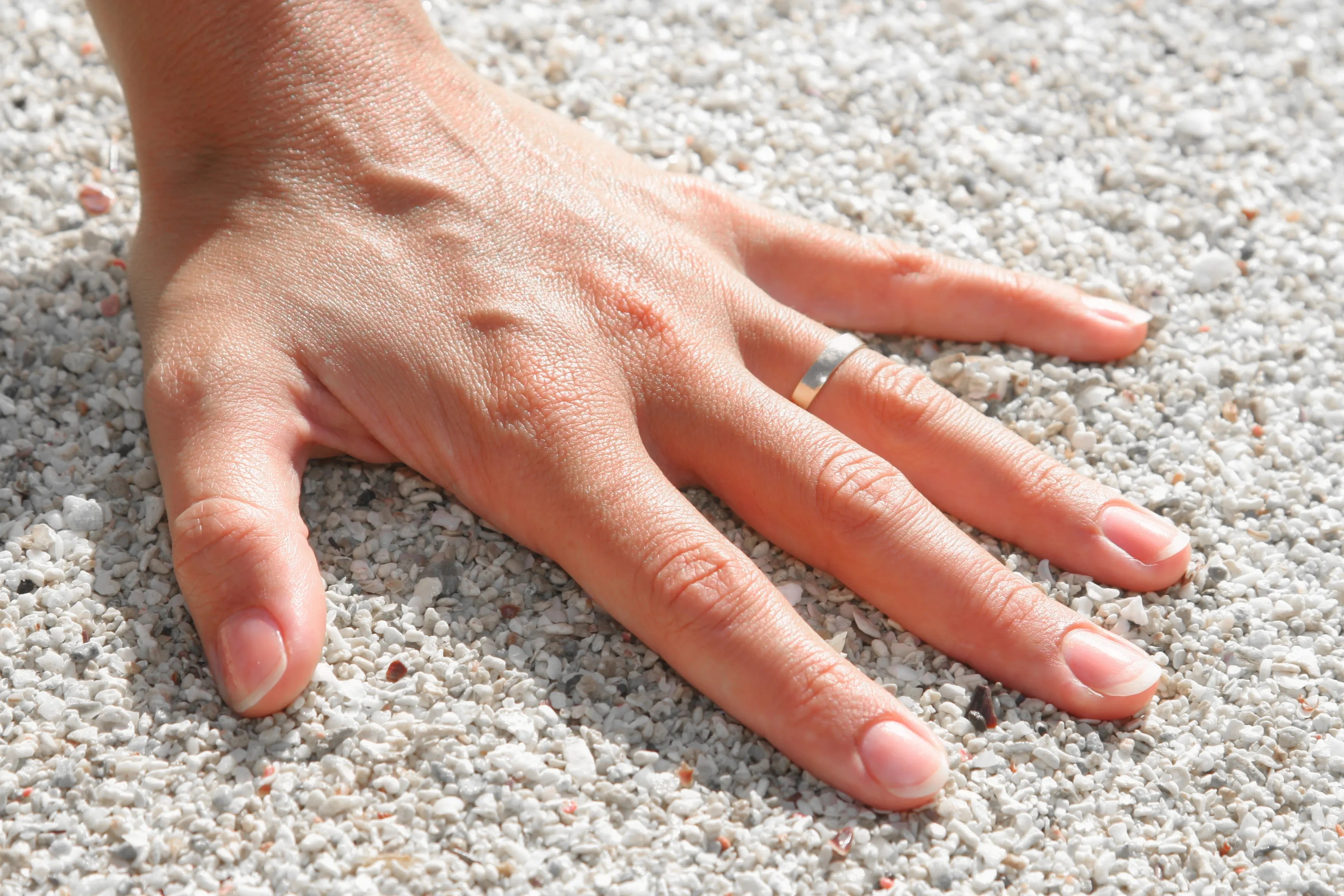 A close-up of a hand resting on white pebbles, wearing a silver ring.