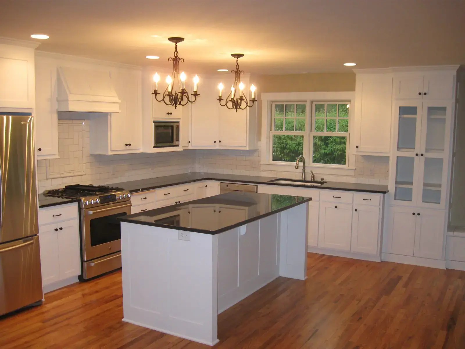 A kitchen in white and stainless steel with enameled cabinets and two chandeliers hanging above the island.