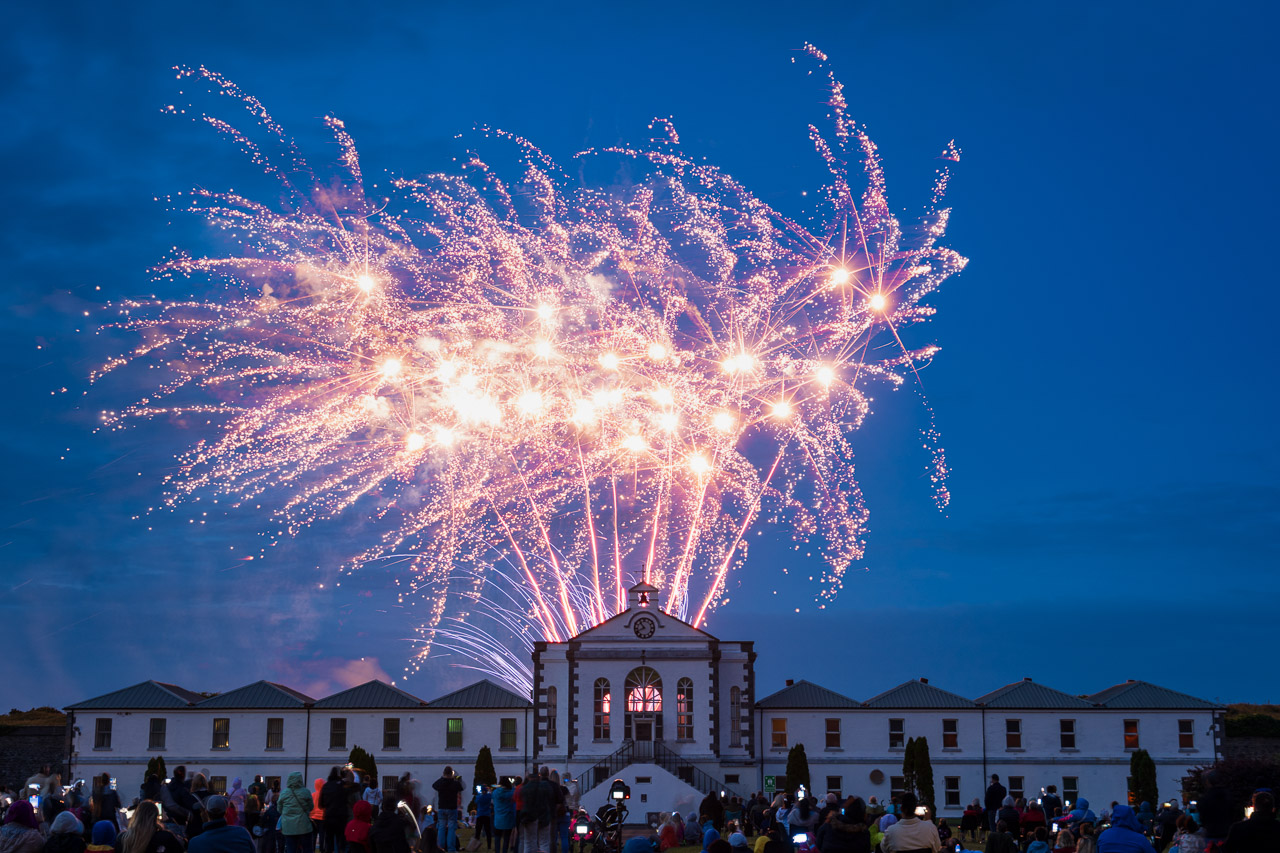 Fireworks light up the sky above Fort Mitchel on Spike Island. a crowd watches, surrounded by the buildings of the fort