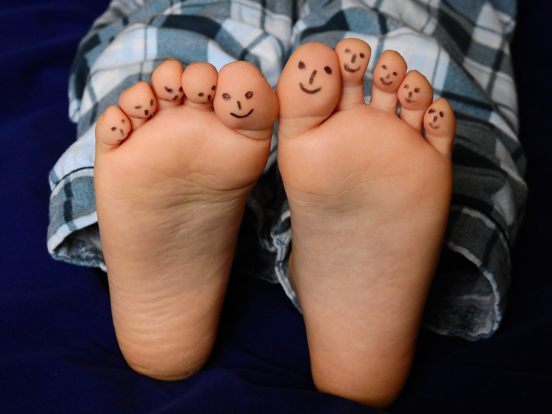 A close-up photo of a child's feet showing the soles, with smiley faces drawn on to each toe in black pen.