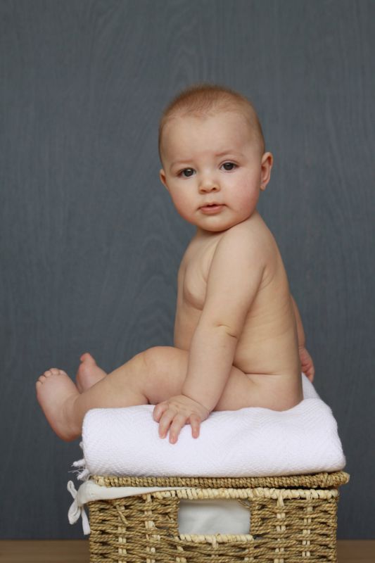A baby sitting on a basket in front of a grey wood backdrop