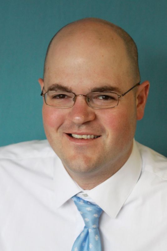 A man wearing glasses and smiling at the camera