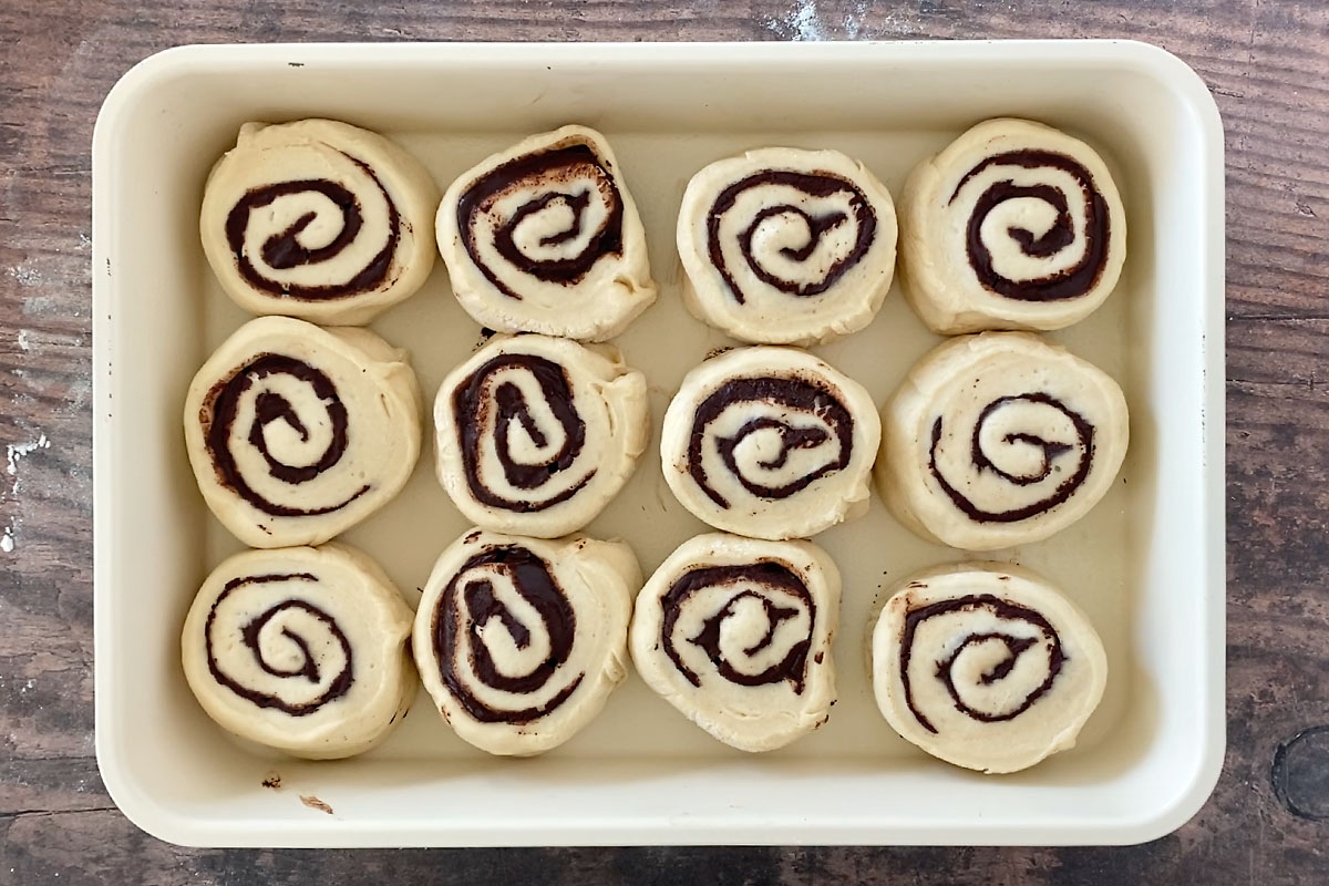 Twelve chocolate babka rolls in a 9x13 pan after rising so rolls are puffed and nearly touching
