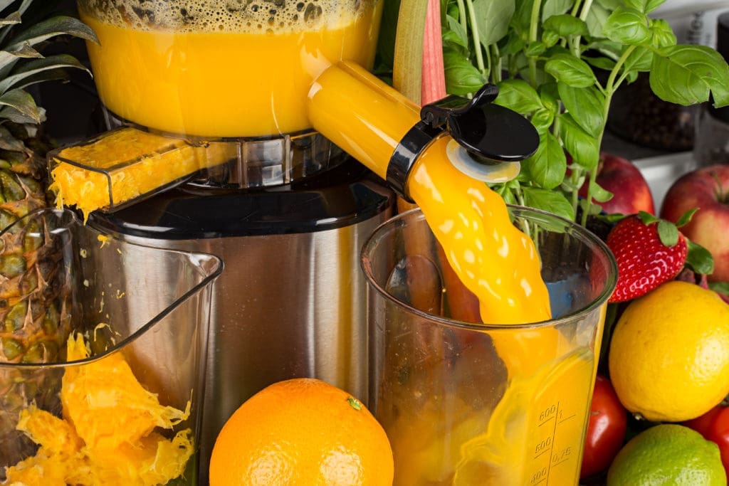 slow juicer in kitchen with many fruit and vegetable orange vitamin