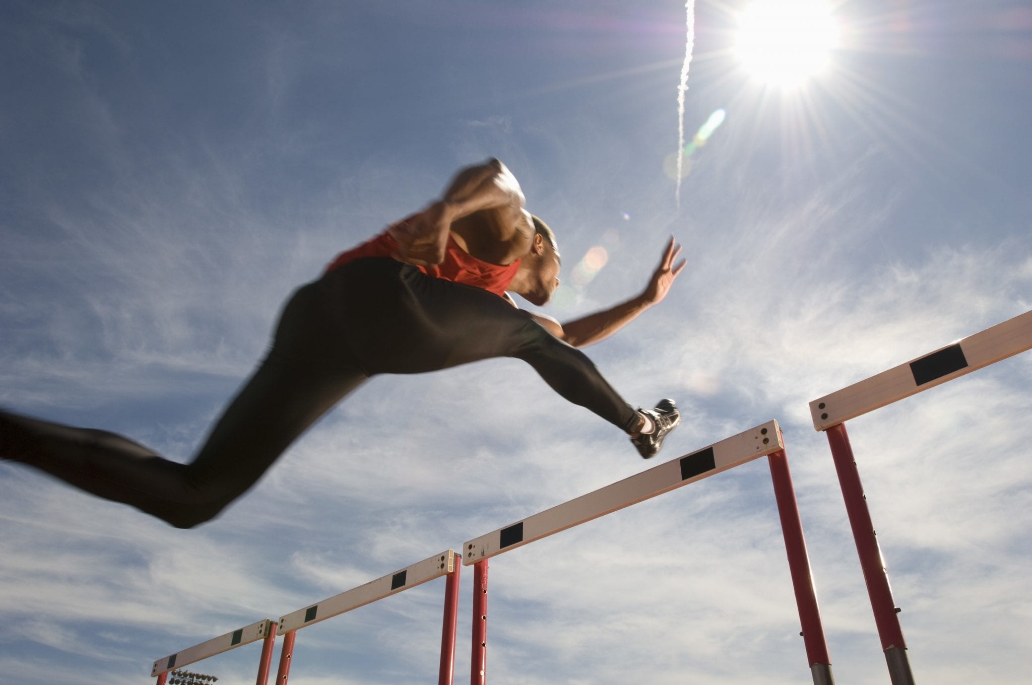 Low angle view of a male athlete jumping hurdle against the sky Juke