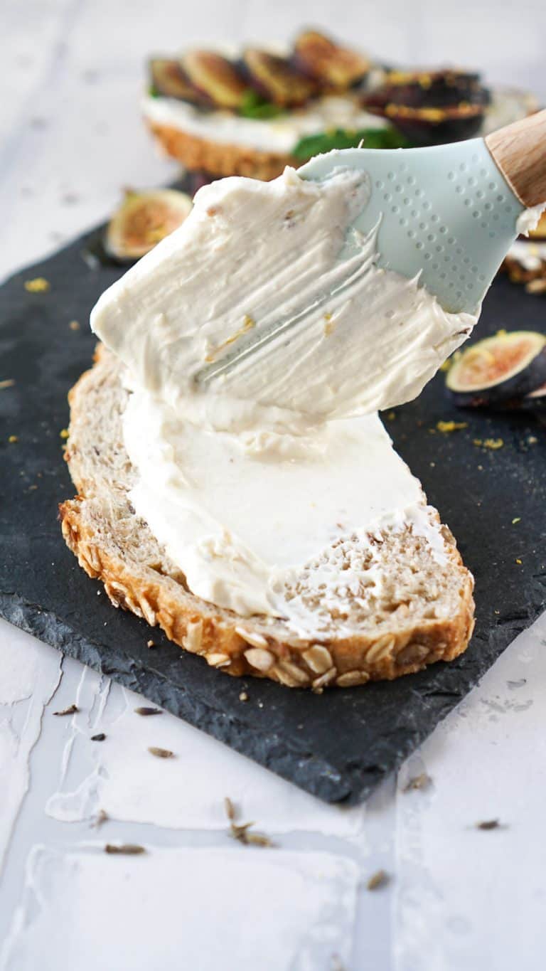 a spatula spreading goat cheese on a piece oftoast
