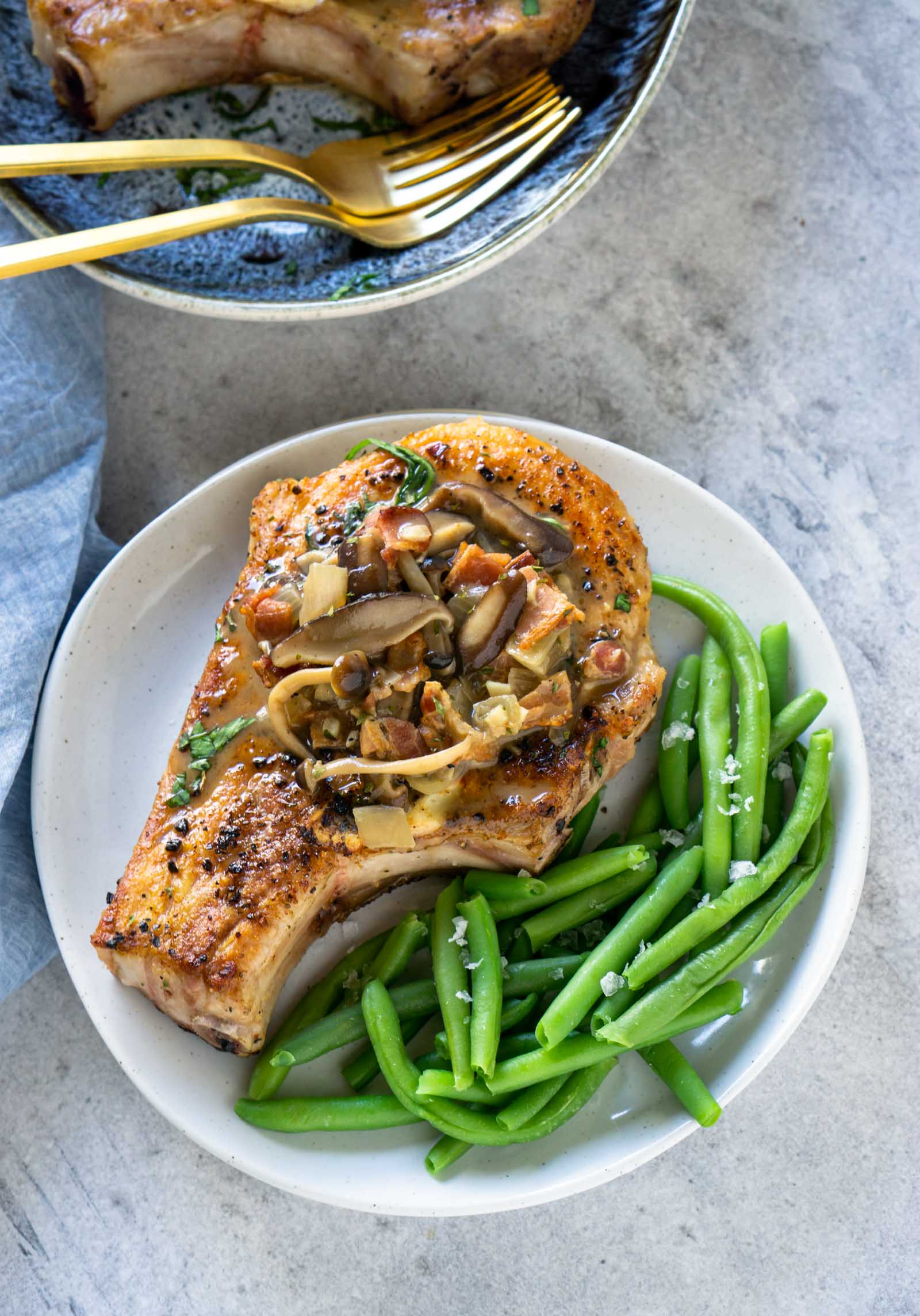 A pork chop on a white plate with green beans