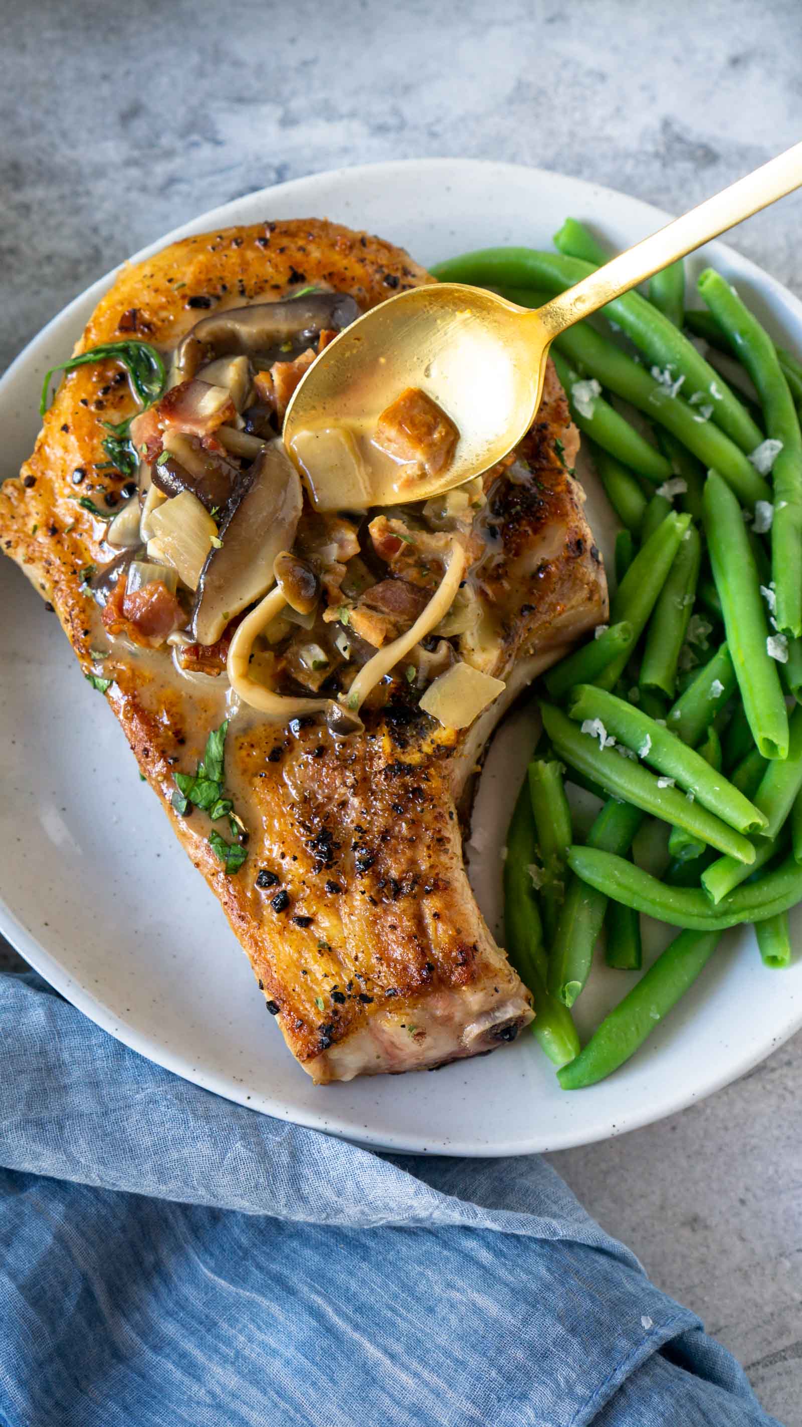 A gold spoon putting bacon mushroom sauce on a pork chop 