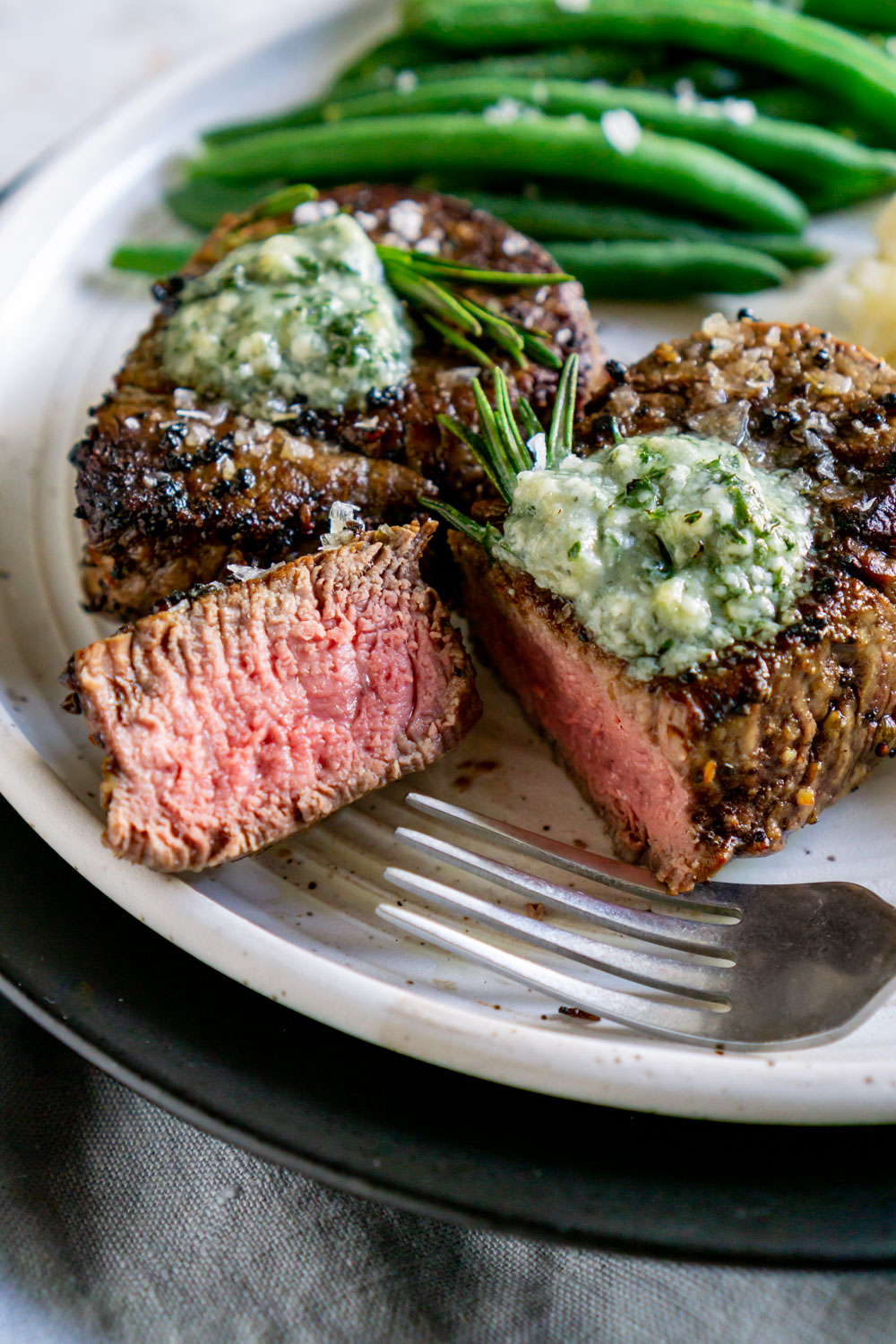 sliced filet mignon on a plate with a fork and green beans