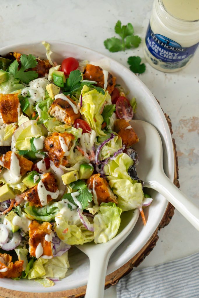 salad in a bowl with tongs and dressing on the side