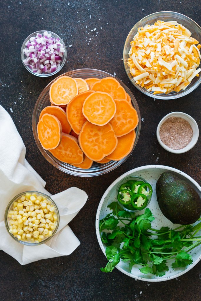 ingredients in small bowls: sliced potatoes, shredded cheese, red onion, cilantro, corn